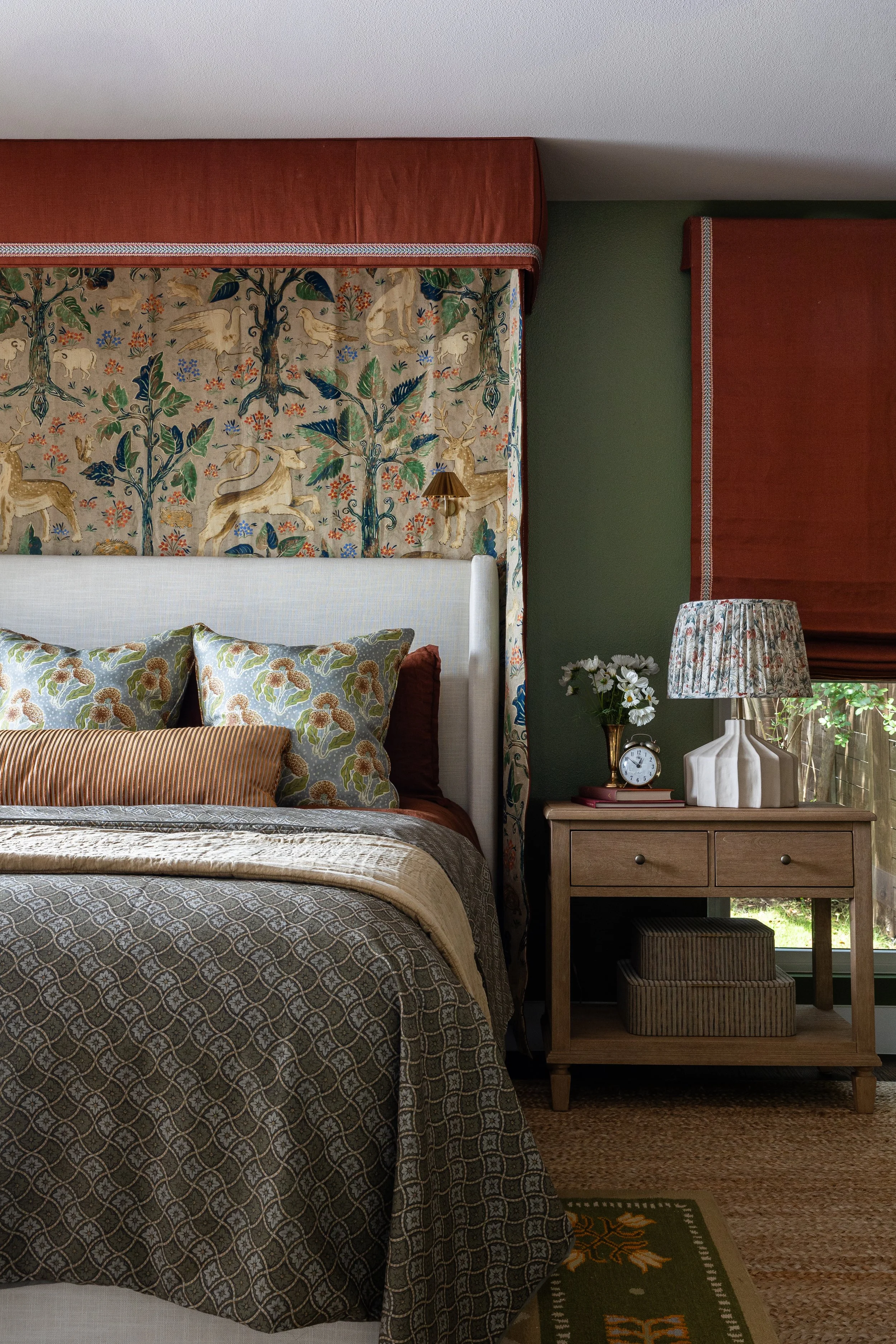 Bedside details in the primary bedroom of this Dallas cottage interior - a botanical canopy, a ceramic lamp with gathered shade, and a simple alarm clock that grounds the room in everyday warmth.