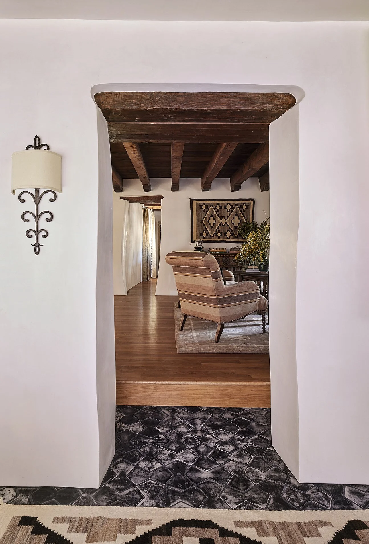 Adobe archway leads into Applegate Estate living room, showcasing exposed beams, black-and-white patterned tile flooring, and Southwestern decor.