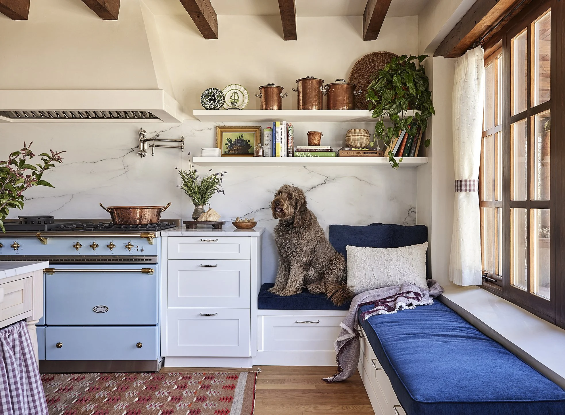Southwestern kitchen showcasing copper cookware, white cabinetry, blue seating nook, and a window seat with throw pillows.