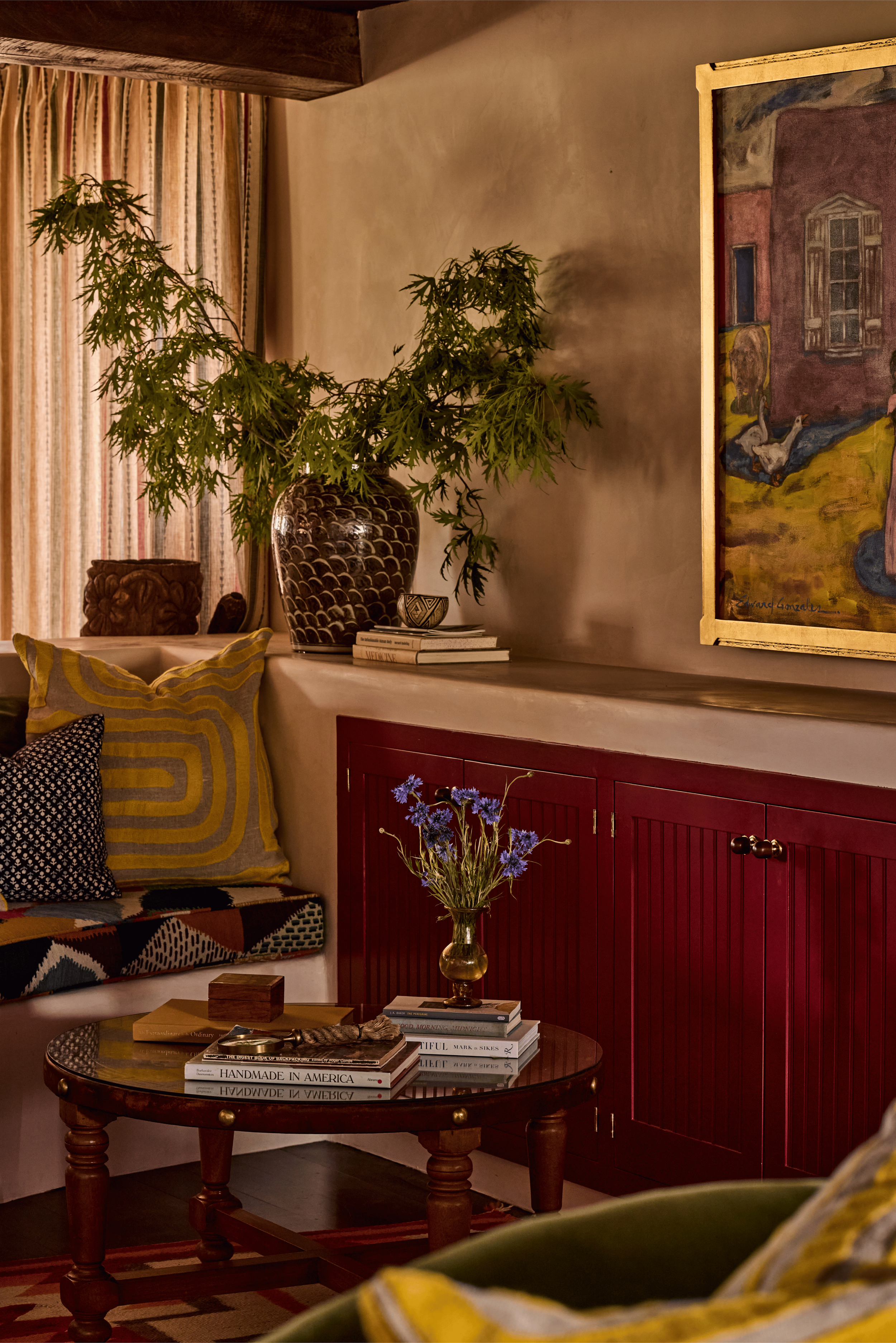 The living room at the Mesa Project reads as a full composition - warm plaster walls, deep red built-ins, a gold-framed oil painting, and layered textiles in mustard and indigo. This is the colorful, soulful Southwest escape French & French Interiors