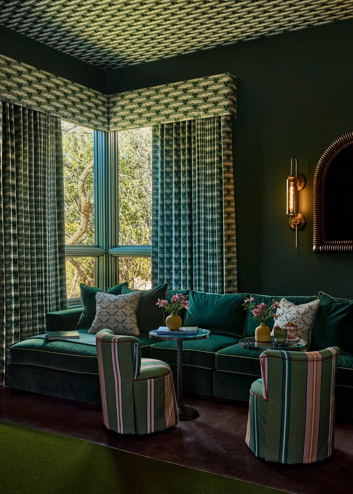 A sophisticated lounge space designed by a Santa Fe interior designer, featuring deep green walls, custom upholstered seating, and layered textiles. The space reflects a maximalist yet refined interior design approach, balancing bold color with comfo