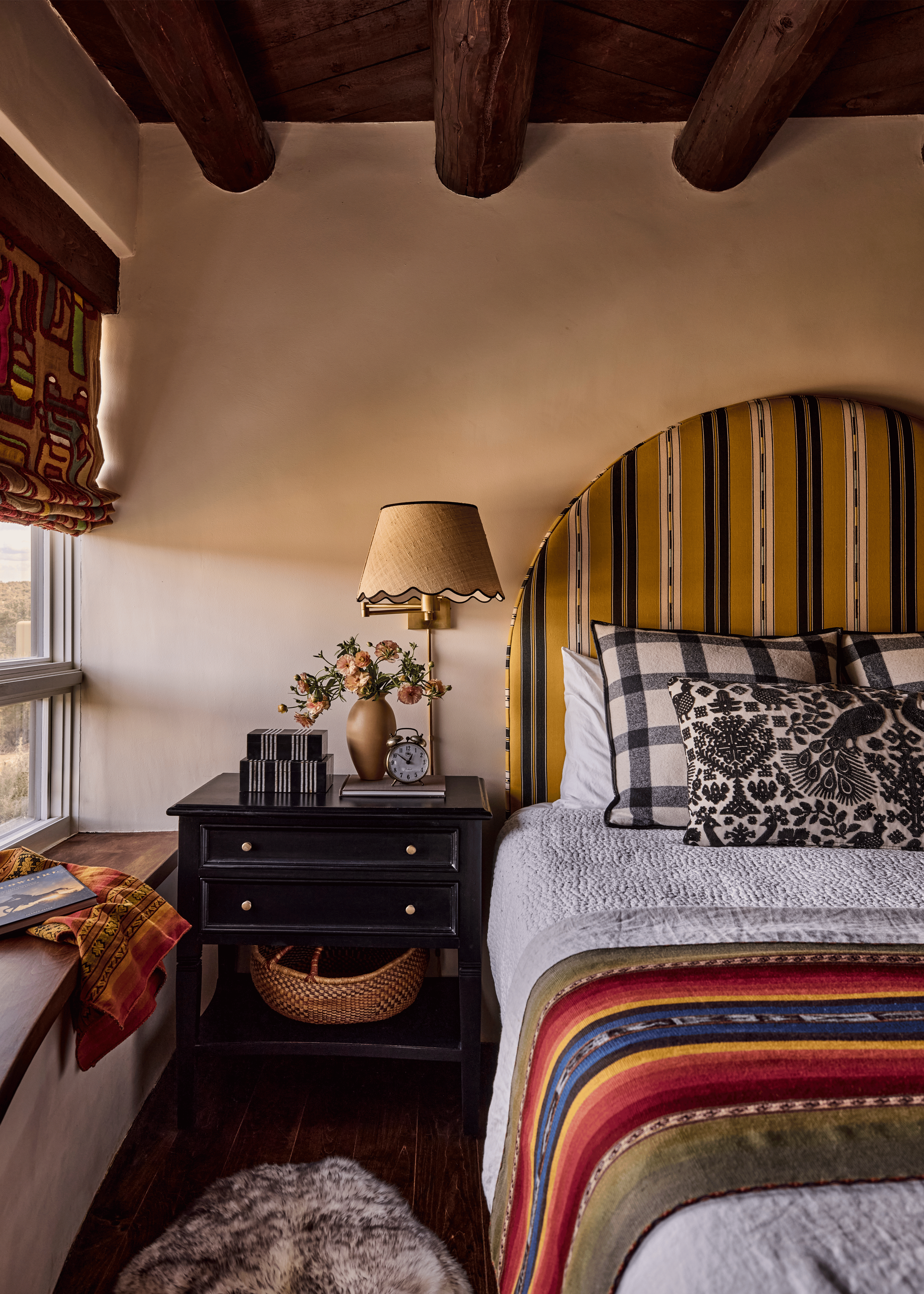 A mustard-striped arched headboard, a traditional Saltillo-style blanket, and a bold folk-print roman shade make this bedroom at the Mesa Project one of the most visually layered rooms in the house - a signature French & French Interiors approach to 
