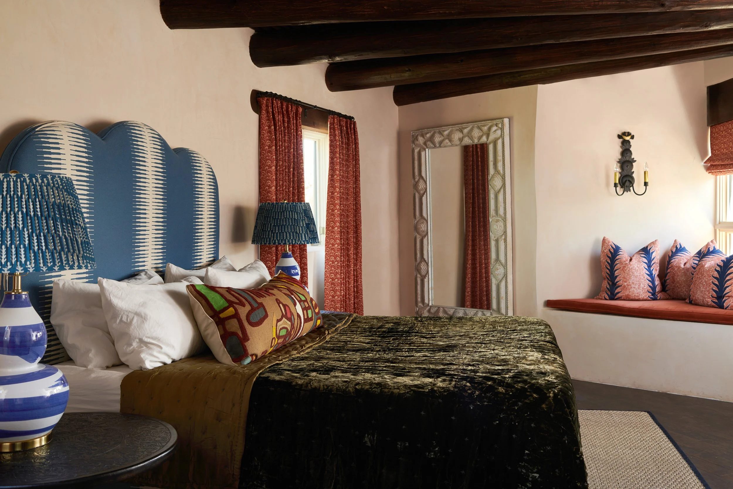Bedroom with a curved blue upholstered headboard, layered pillows, and textured bedding in deep jewel tones.