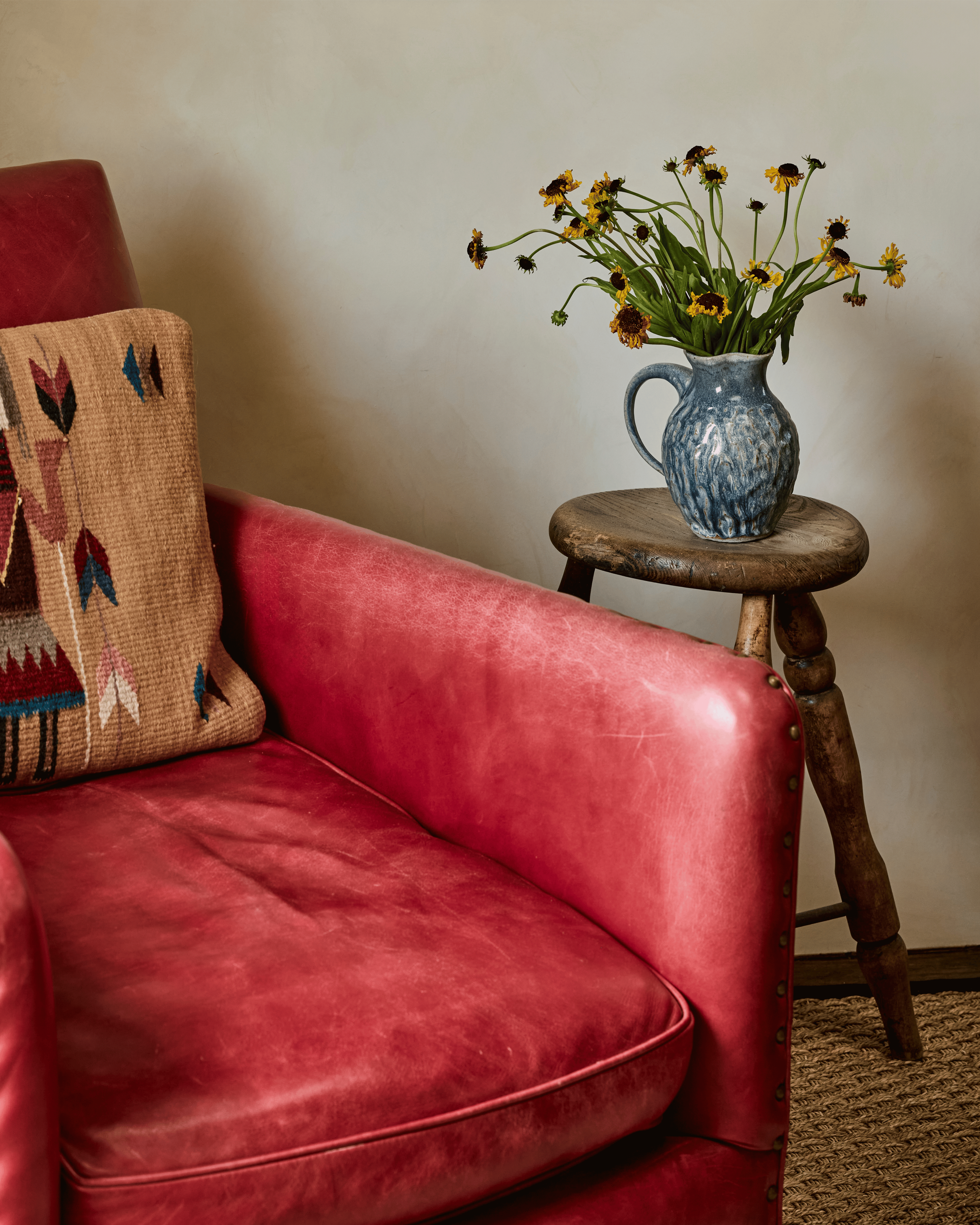 A worn red leather chair, a woven geometric pillow, and a blue ceramic pitcher of desert wildflowers on a turned wood stool - this detail shot from the Mesa Project captures the way French & French Interiors layers material, color, and craft into som