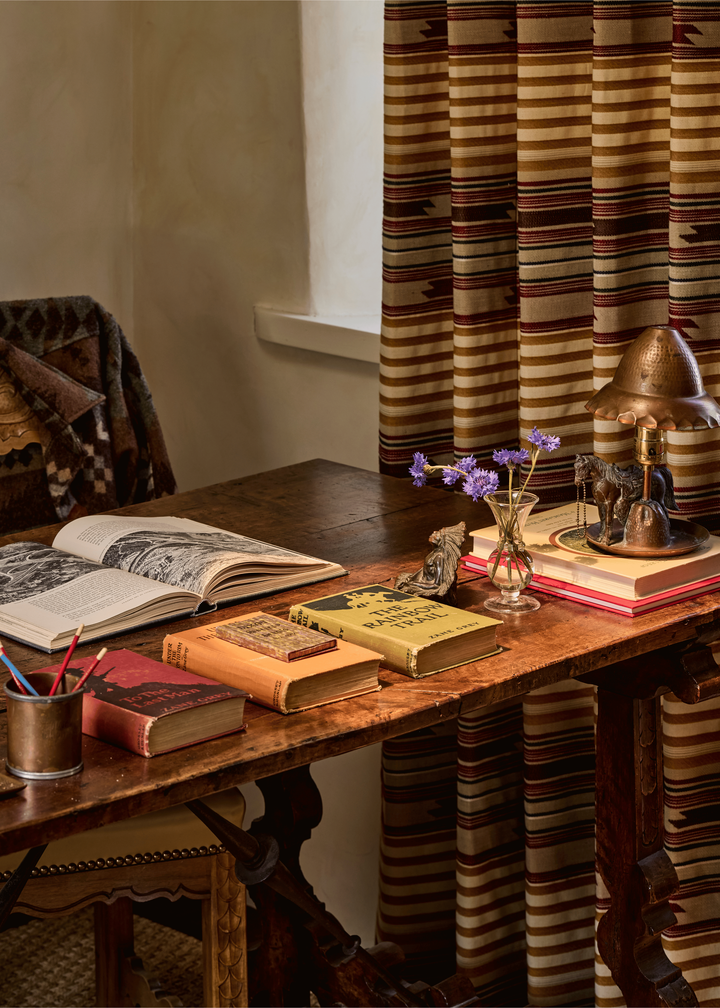 An antique writing desk in the Mesa Project's study holds vintage Zane Grey novels, a copper lamp, and a small glass vase of wildflowers - objects chosen by French & French Interiors that speak directly to the landscape and literary history of northe
