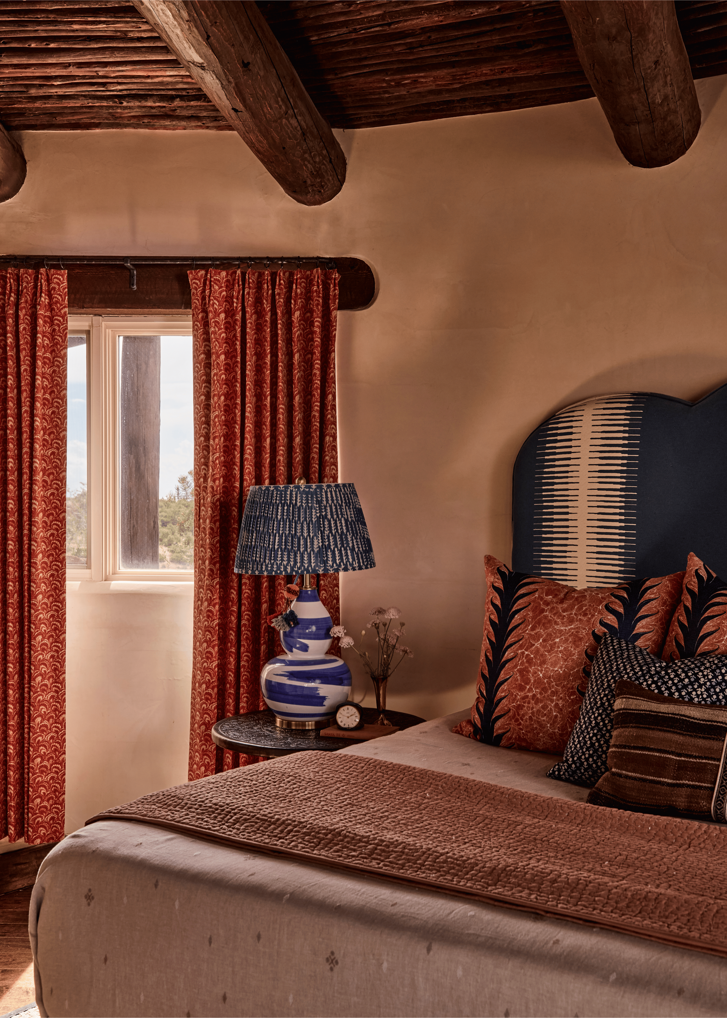 Rust red block-print drapes, a navy arched headboard inlaid with a graphic woven panel, and a blue and white ceramic lamp create a bedroom at the Mesa Project that is layered without being busy - a balance French & French Interiors reaches through pr