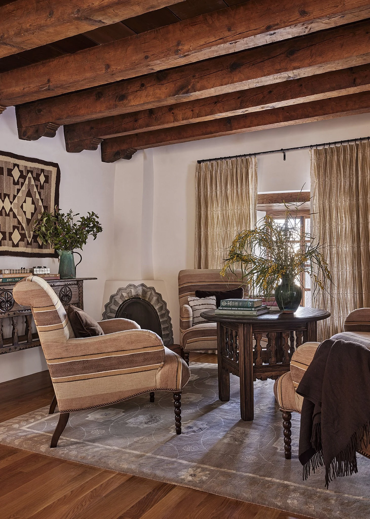 Cozy living space at Applegate Estate featuring striped armchairs, a wood coffee table, greenery accents, and traditional Southwestern wall weaving under exposed beams.