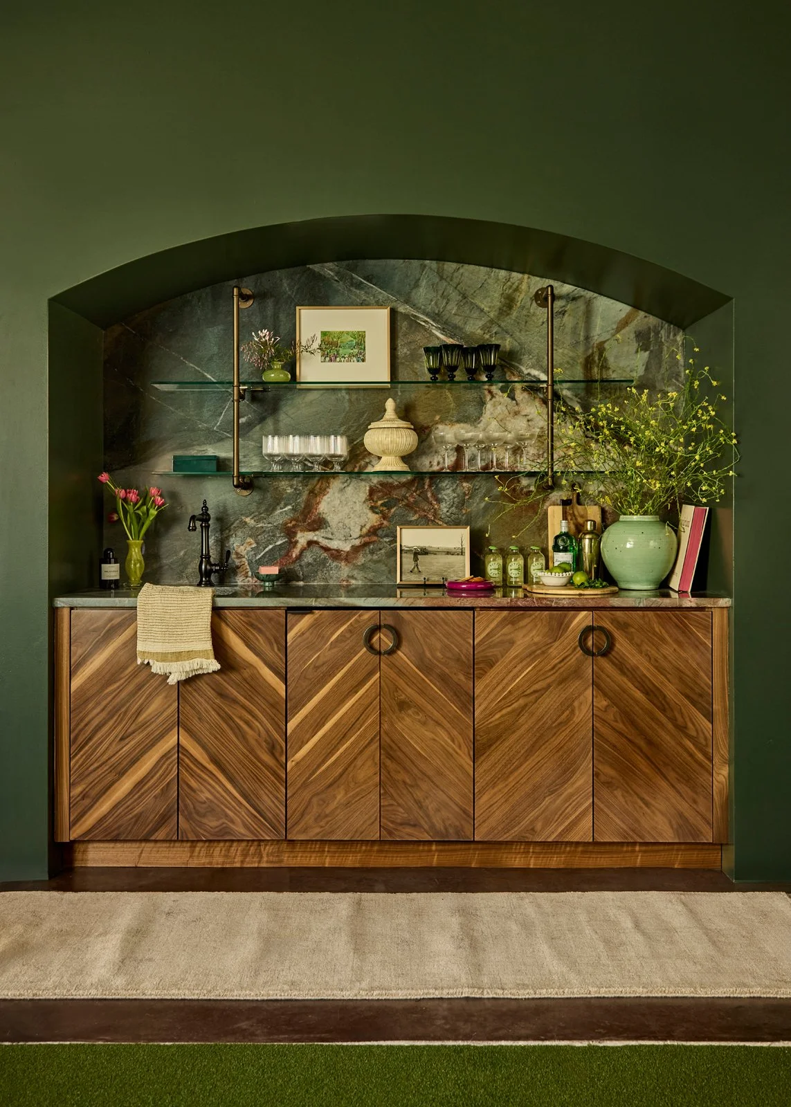 A custom arched bar designed by a Santa Fe interior designer, featuring chevron-pattern walnut cabinetry and an emerald quartzite backsplash. This hospitality-inspired residential space combines high-end materiality with functional design, creating a
