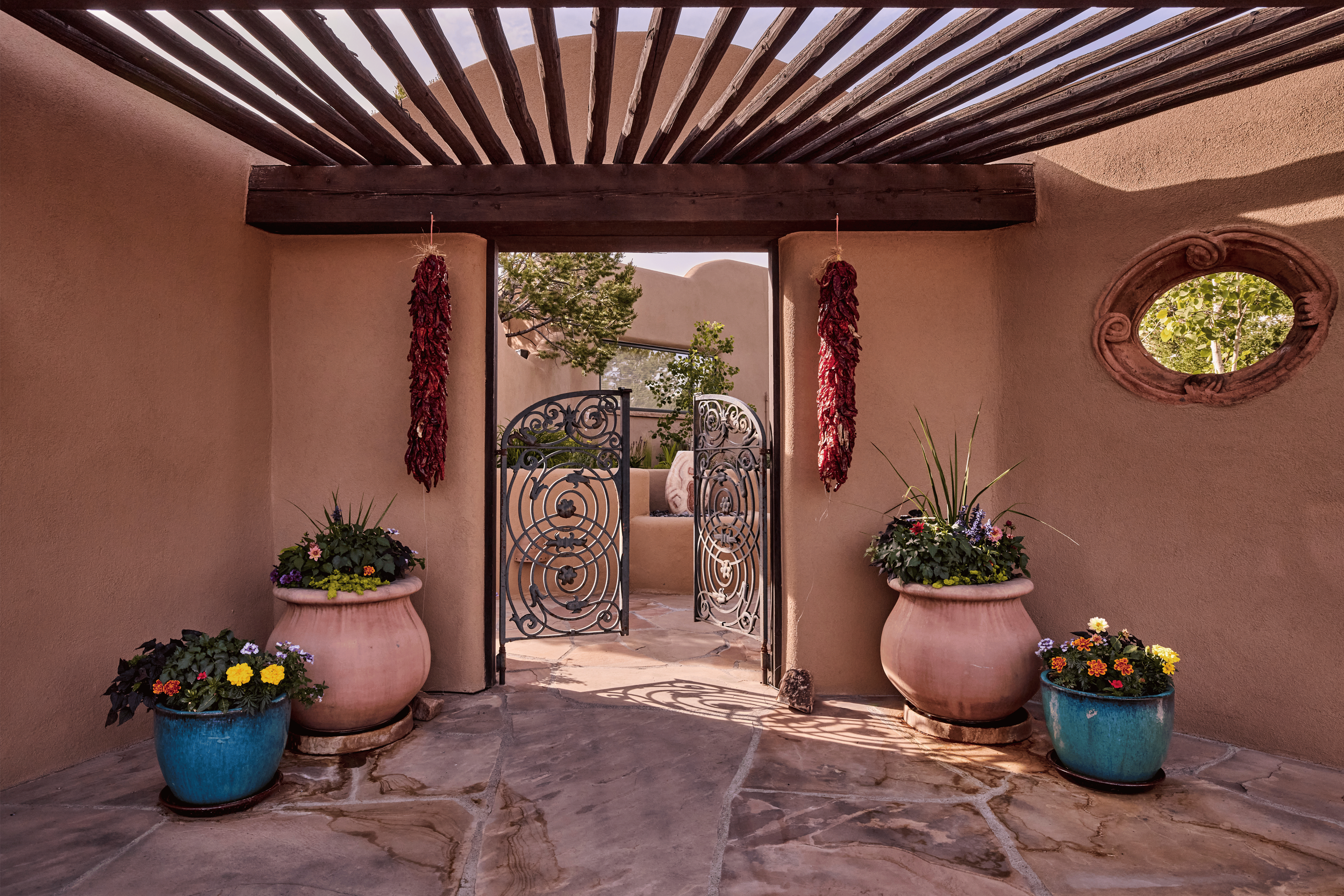 Dried red chile ristras flank a hand-forged iron gate beneath a viga-beamed portal - an entry designed by French & French Interiors that honors the full visual language of traditional New Mexico architecture while feeling completely alive.