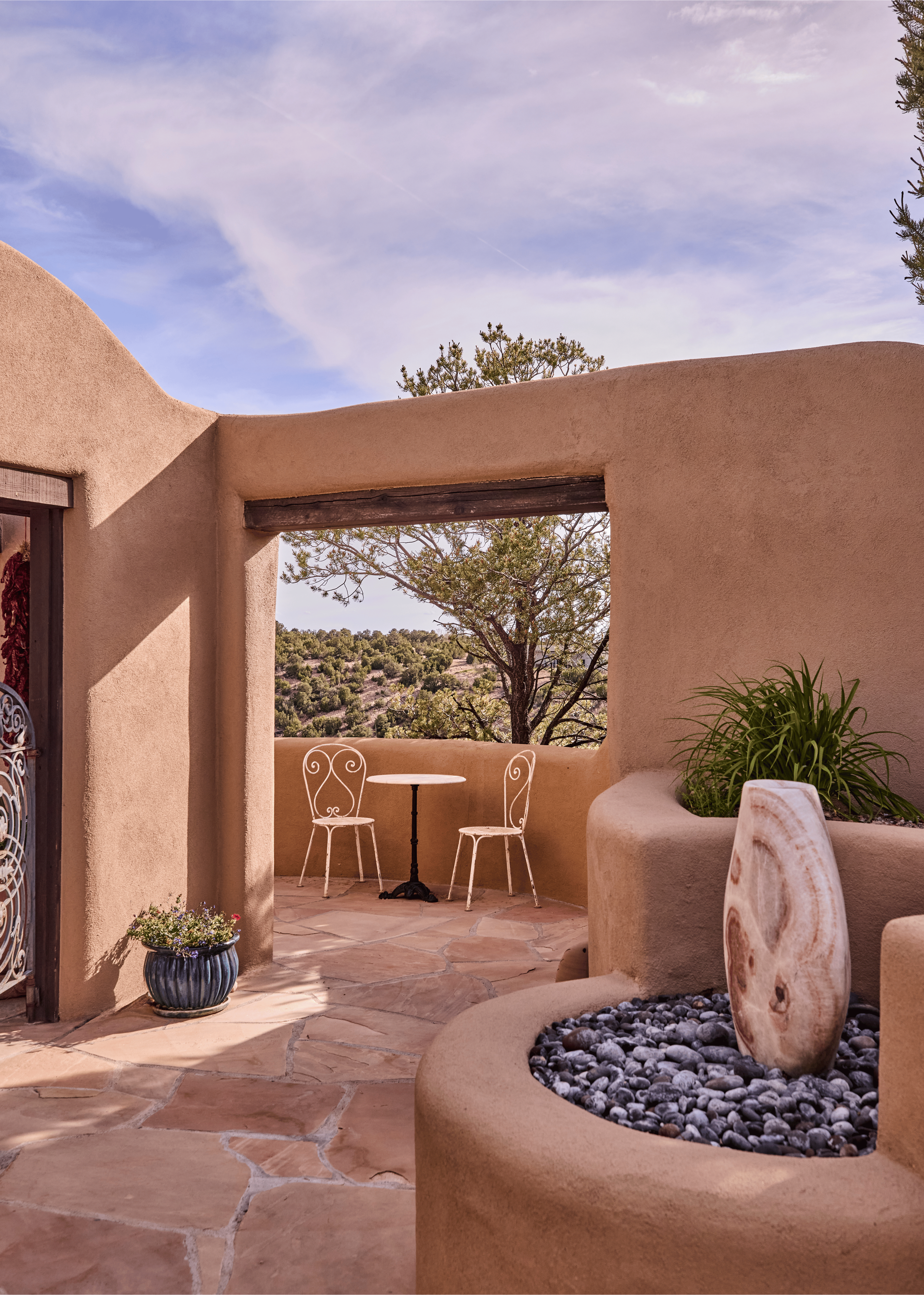 Through the open iron gate, the Mesa Project's terrace and high desert mesa stretch into the distance. French & French Interiors designed the entire arrival sequence - from the stone water feature at the entry to the portal beyond - as a continuous e