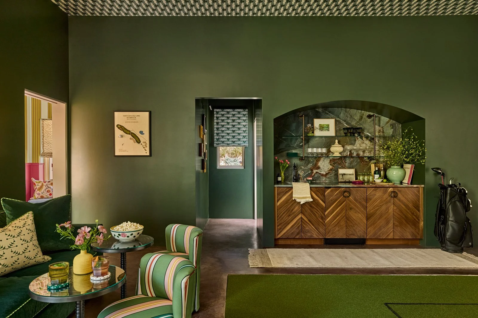 A high-end interior design project in Santa Fe showcasing a custom golf simulator lounge with integrated bar, rich green walls, and layered textures. Designed as a residential entertainment space with a boutique hospitality feel, the room blends tech