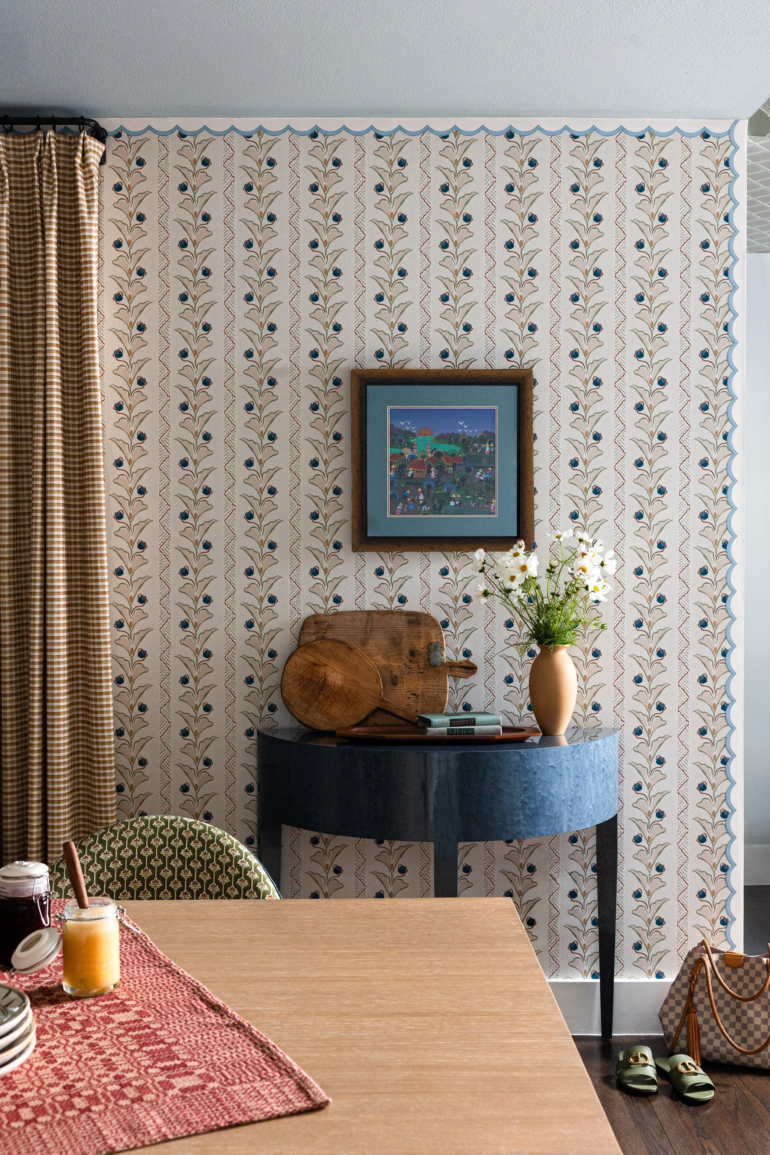 A painted demilune table styled with vintage cutting boards and gathered daisies anchors the dining room wall in this Dallas cottage home - layered, storied, and entirely livable.