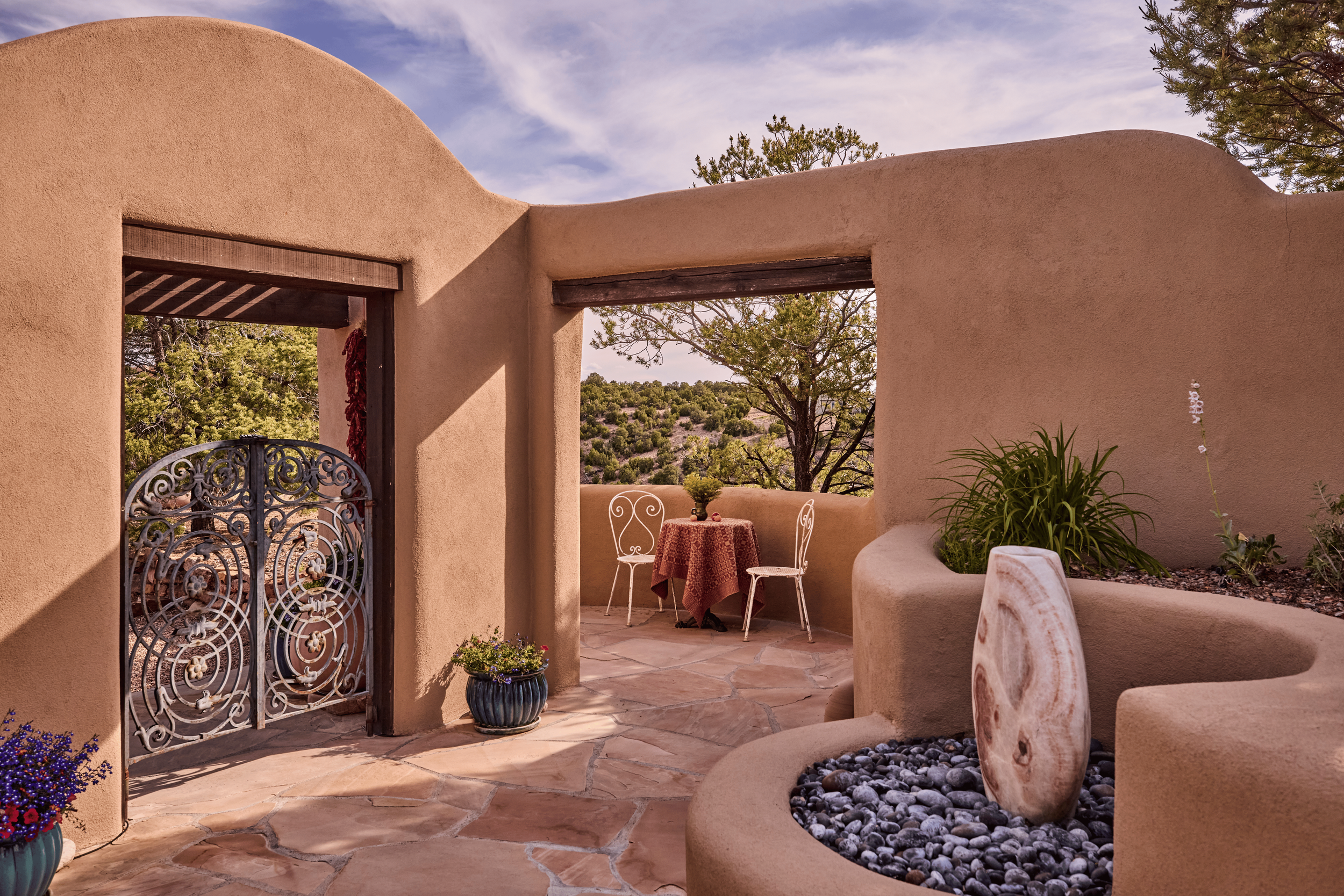 The entry courtyard of the Mesa Project sets the tone: a hand-forged iron gate, a stone water feature, and uninterrupted views of the Tesuque mesa beyond. French & French Interiors designed the full experience of arrival as deliberately as any interi