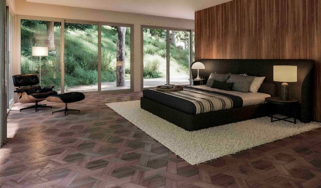 Master bedroom in a Girona forest retreat featuring floor-to-ceiling windows with woodland views, wood paneling, a designer lounge chair, and a minimalist black bed by Sebastian PM
