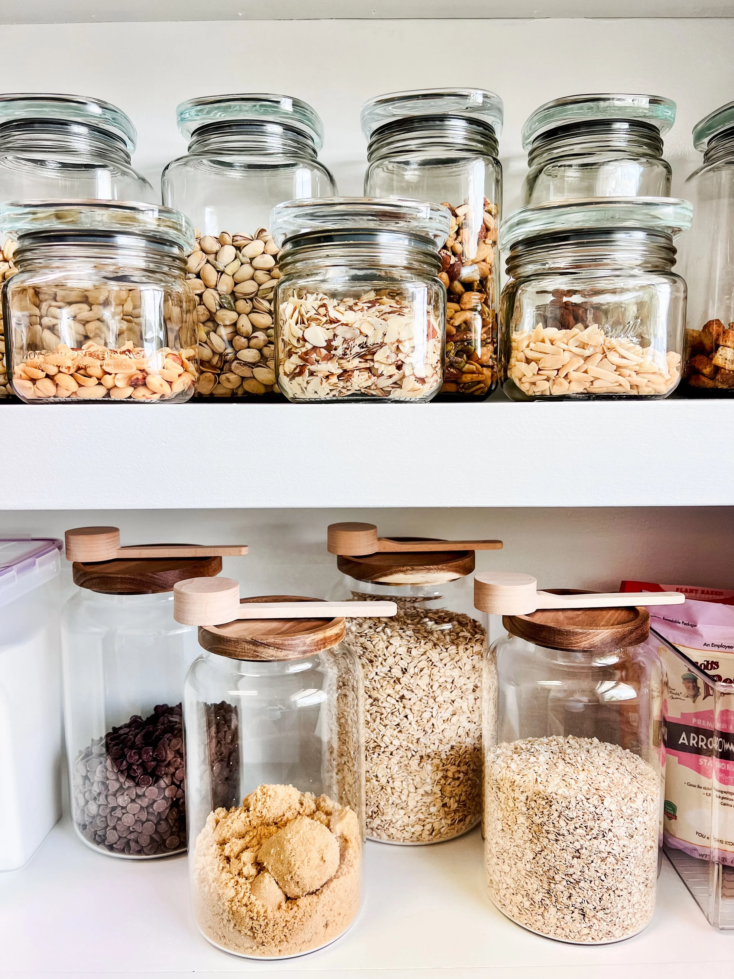 Organized Pantry shelves with cookbooks, glass jars with grains and baking supplies, plastic containers for flour, and organized baking ingredients on the bottom shelf.