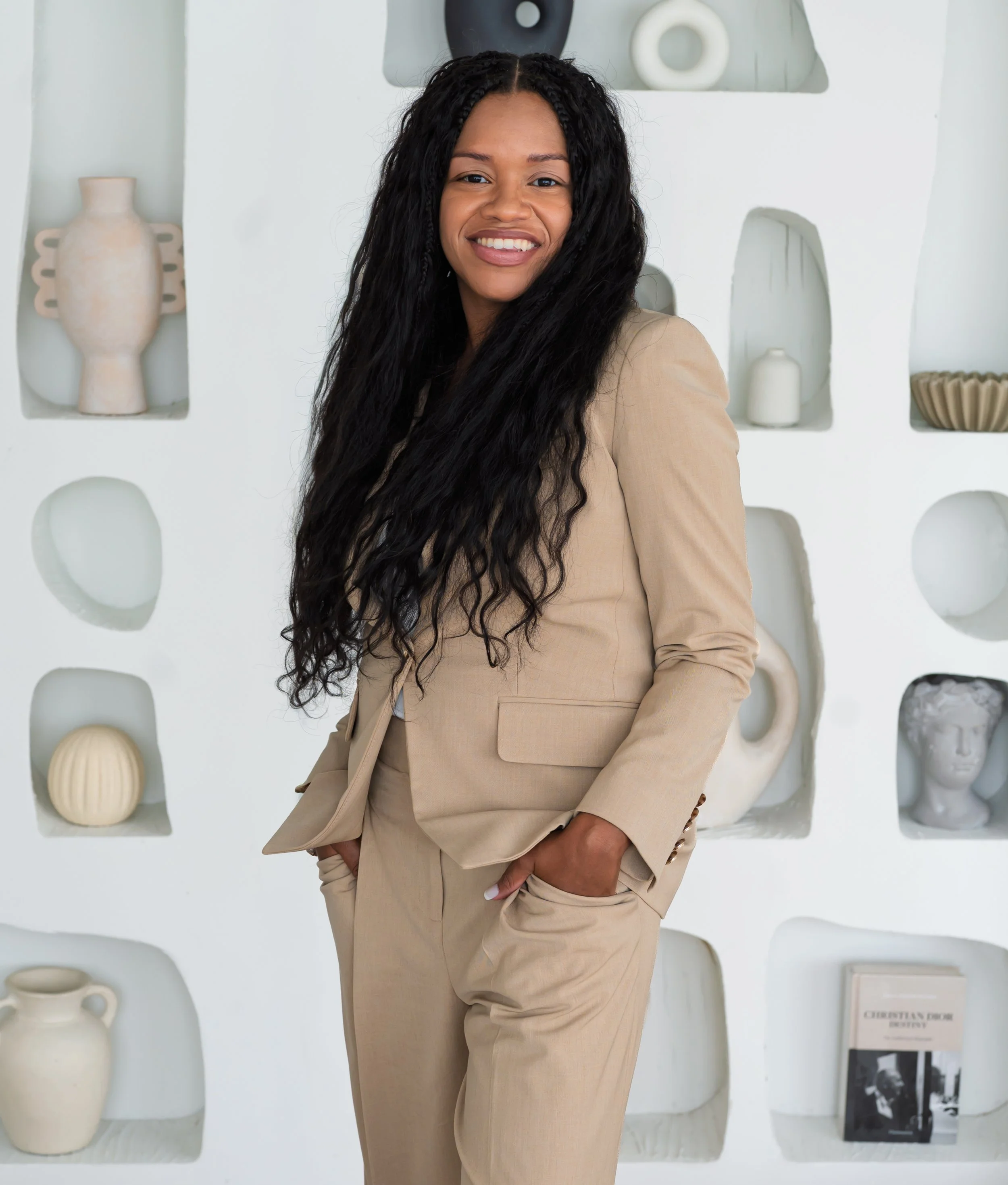 Sowania Germain, postpartum therapist in West Palm Beach, smiling in a tan suit in front of a sculpted shelf wall