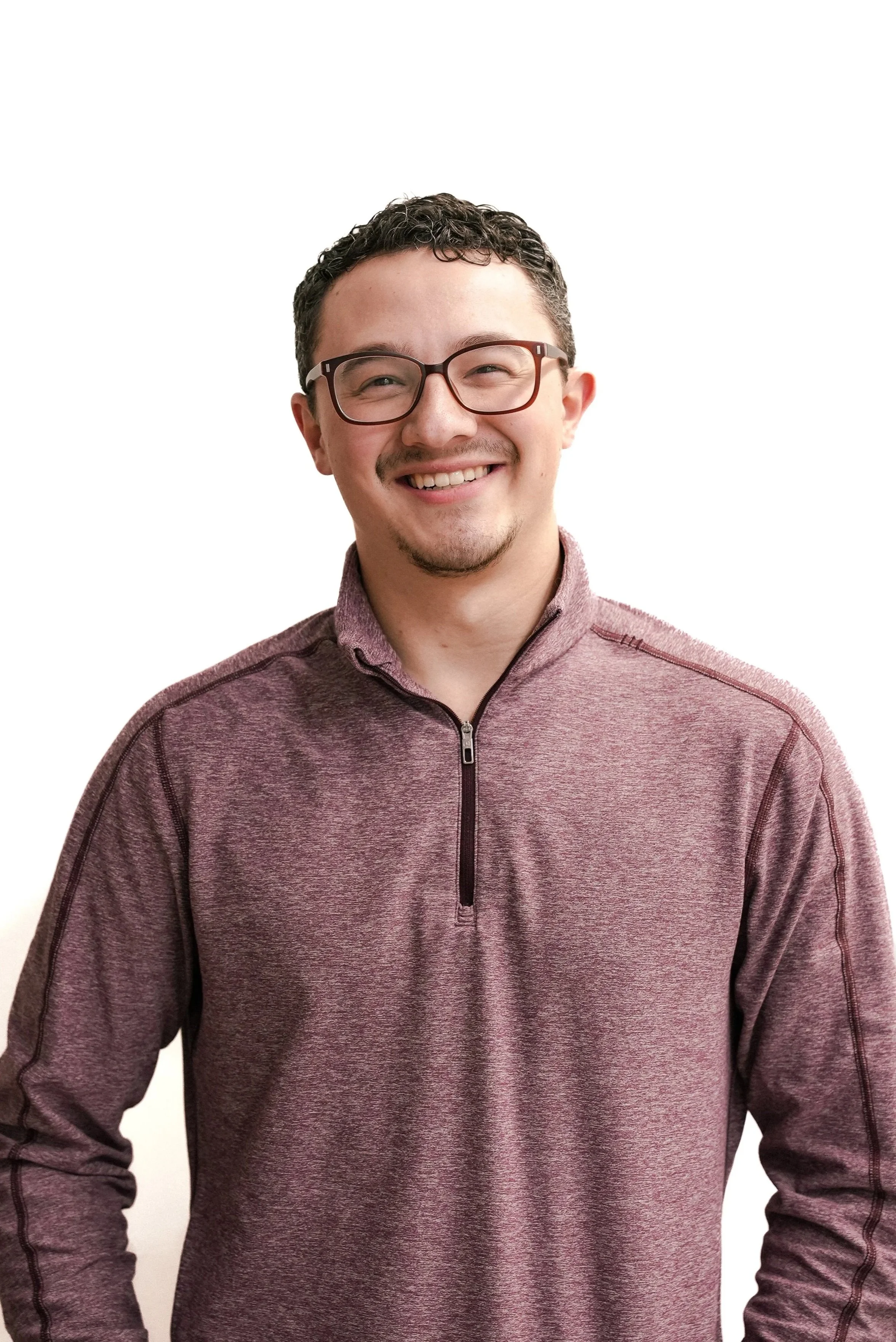 A young man smiling, wearing glasses and a maroon quarter-zip pullover against a plain white background.