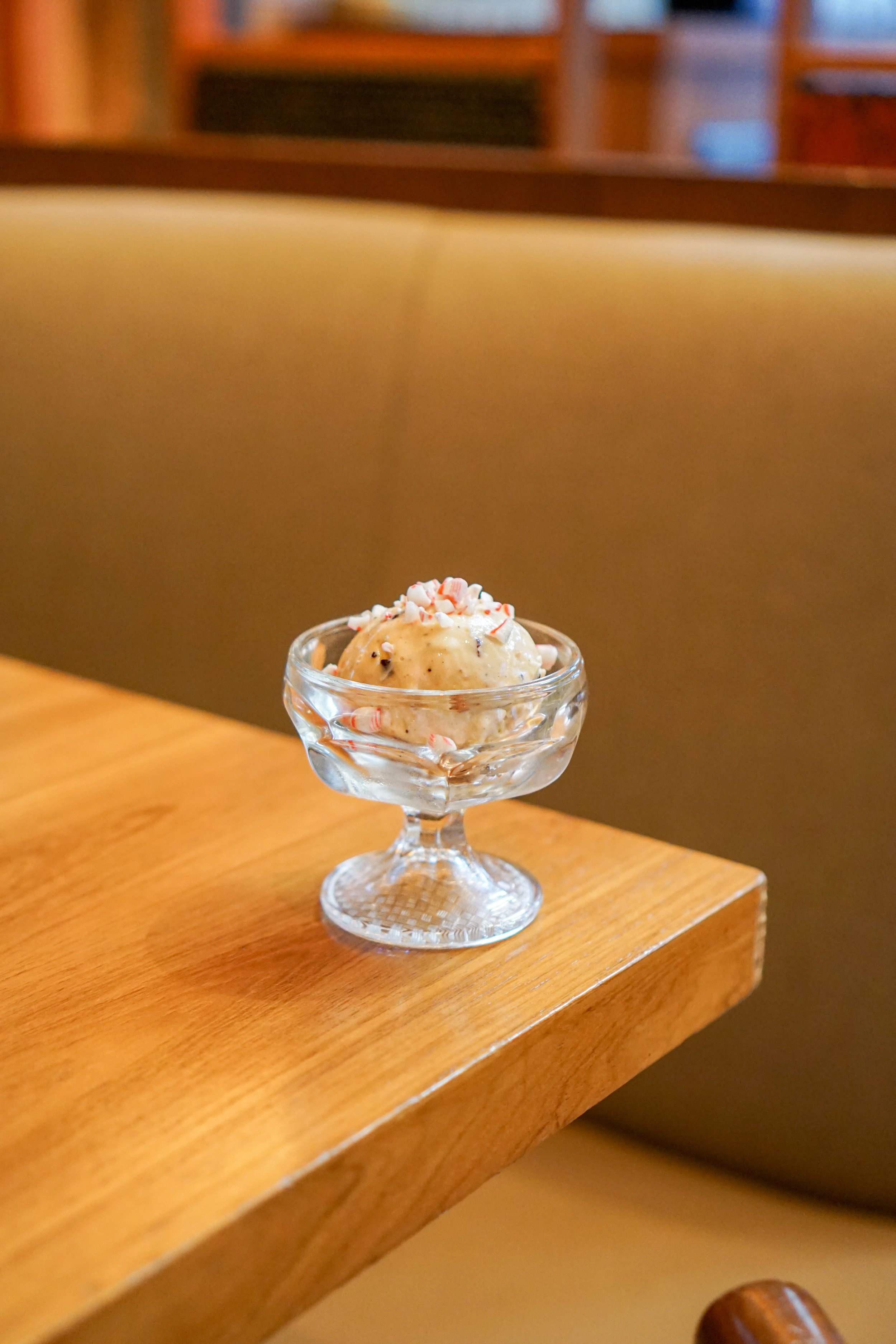 A small glass dish of ice cream with crushed peppermint topping on a wooden table.