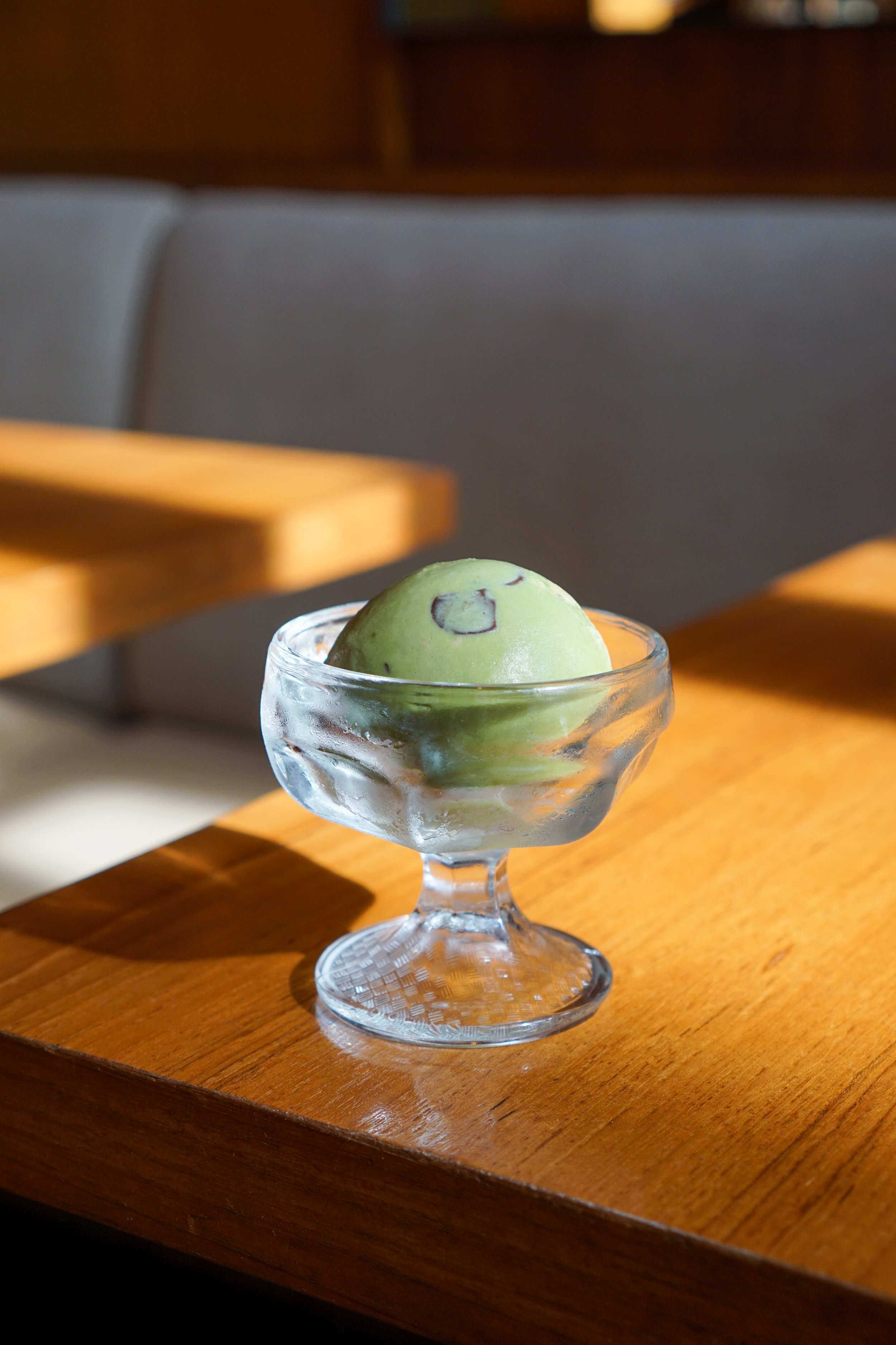 A scoop of green ice cream with chocolate chips in a glass dessert cup on a wooden table