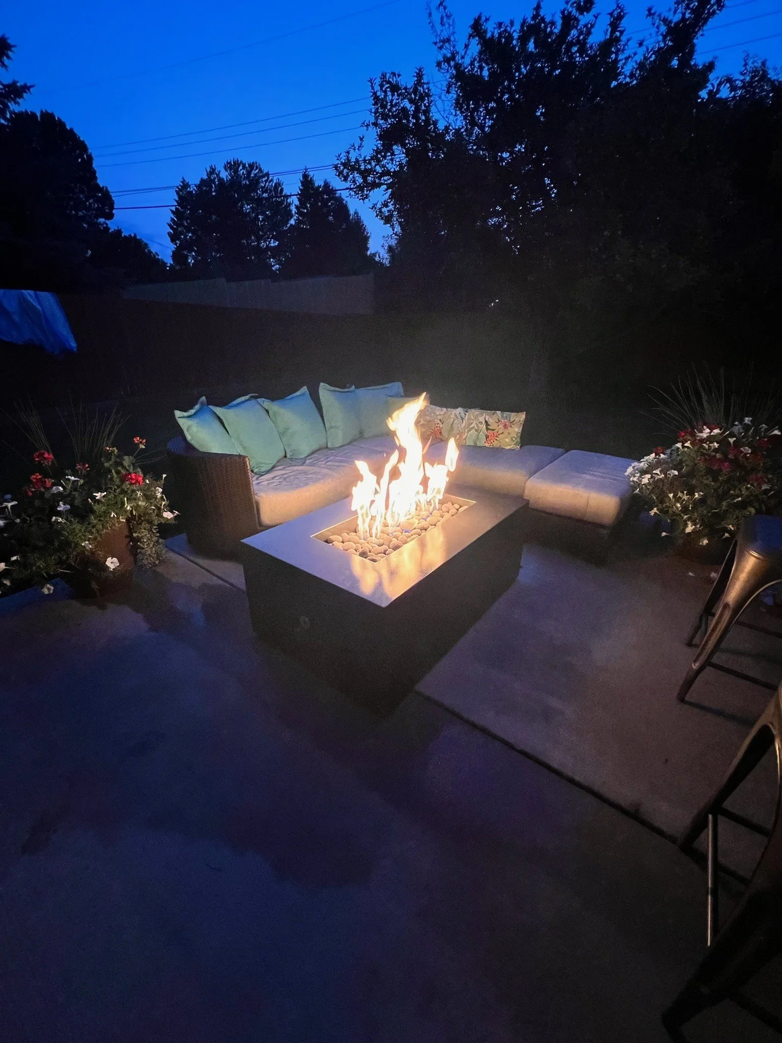Nighttime outdoor patio with a fire feature, cushioned sectional sofa, decorative pillows, and potted flowers.