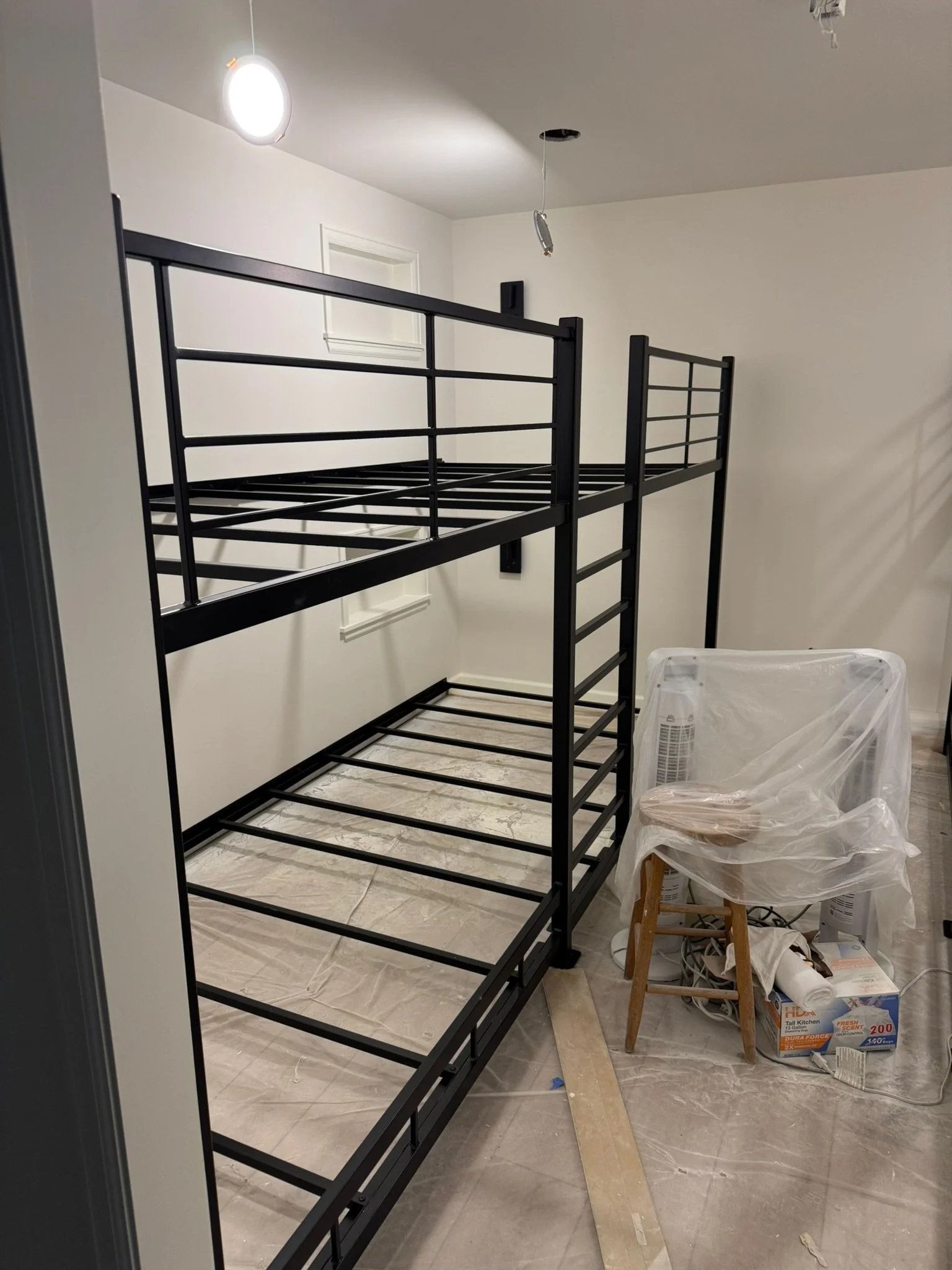 Black metal bunk bed frame in a room under construction, with tools and supplies nearby.