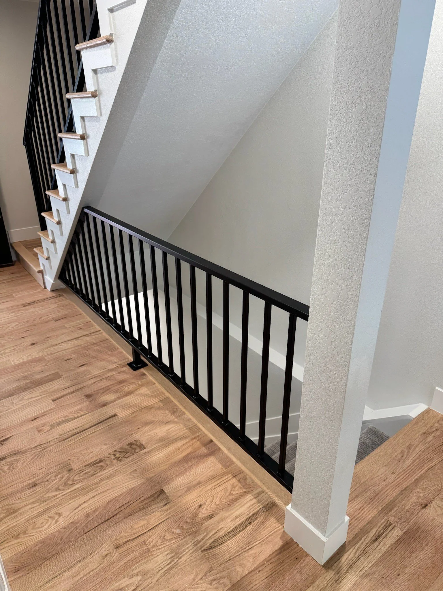 Interior view of a staircase with black metal railing, wooden stairs and flooring, and white walls.