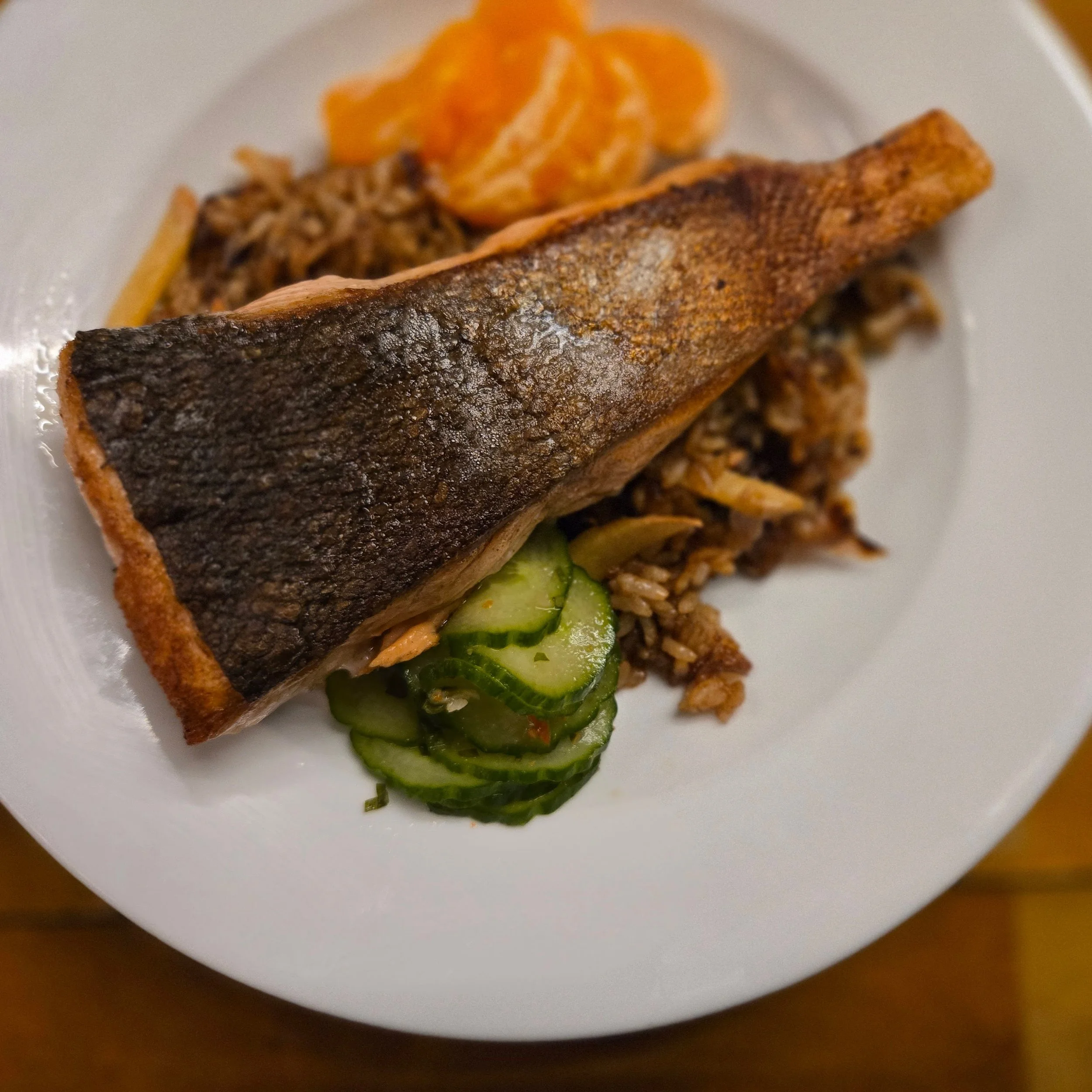 Plate with sockeye salmon fillet, sliced cucumbers, cooked rice, and sliced oranges.