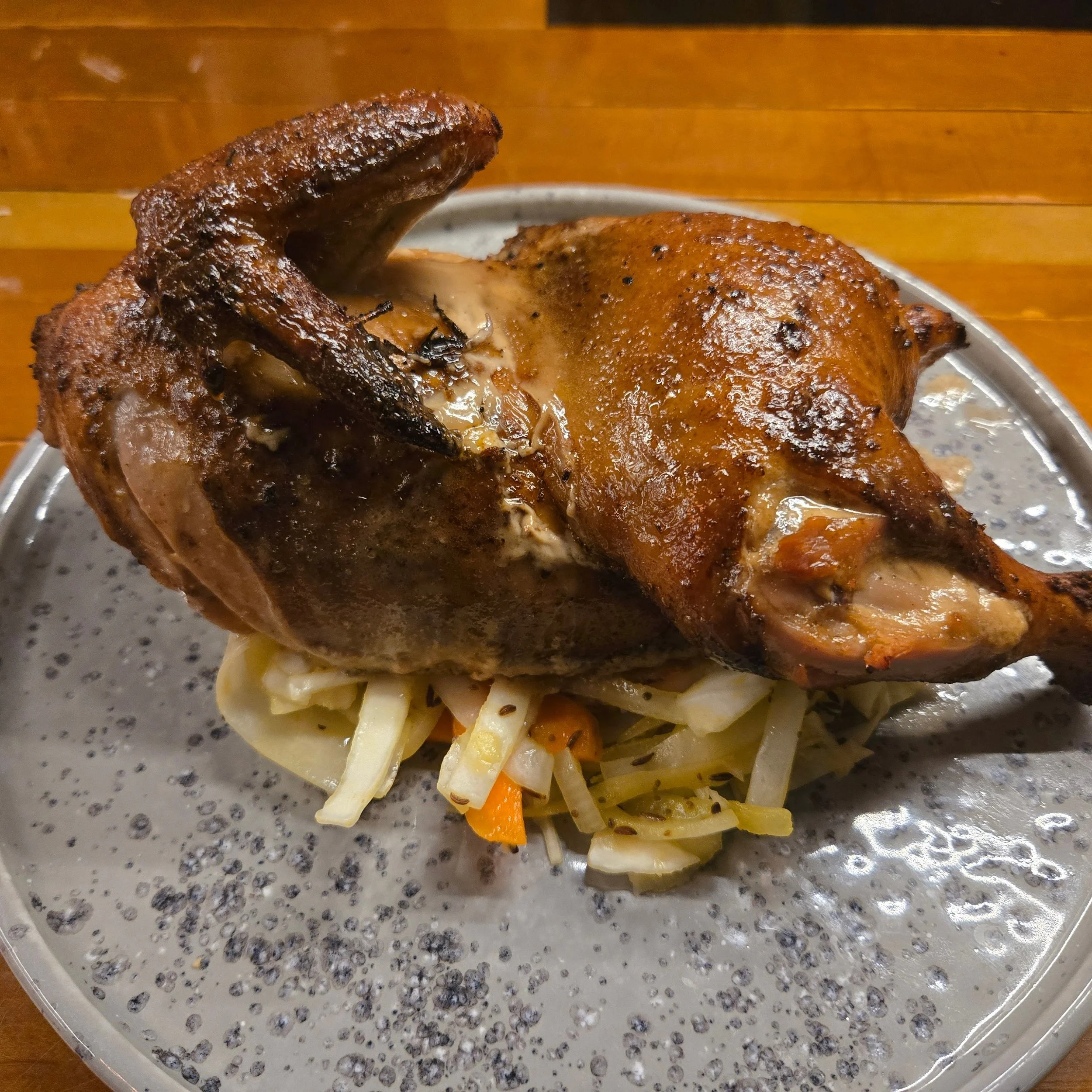 Roast chicken served on a bed of cooked vegetables on a speckled gray plate.