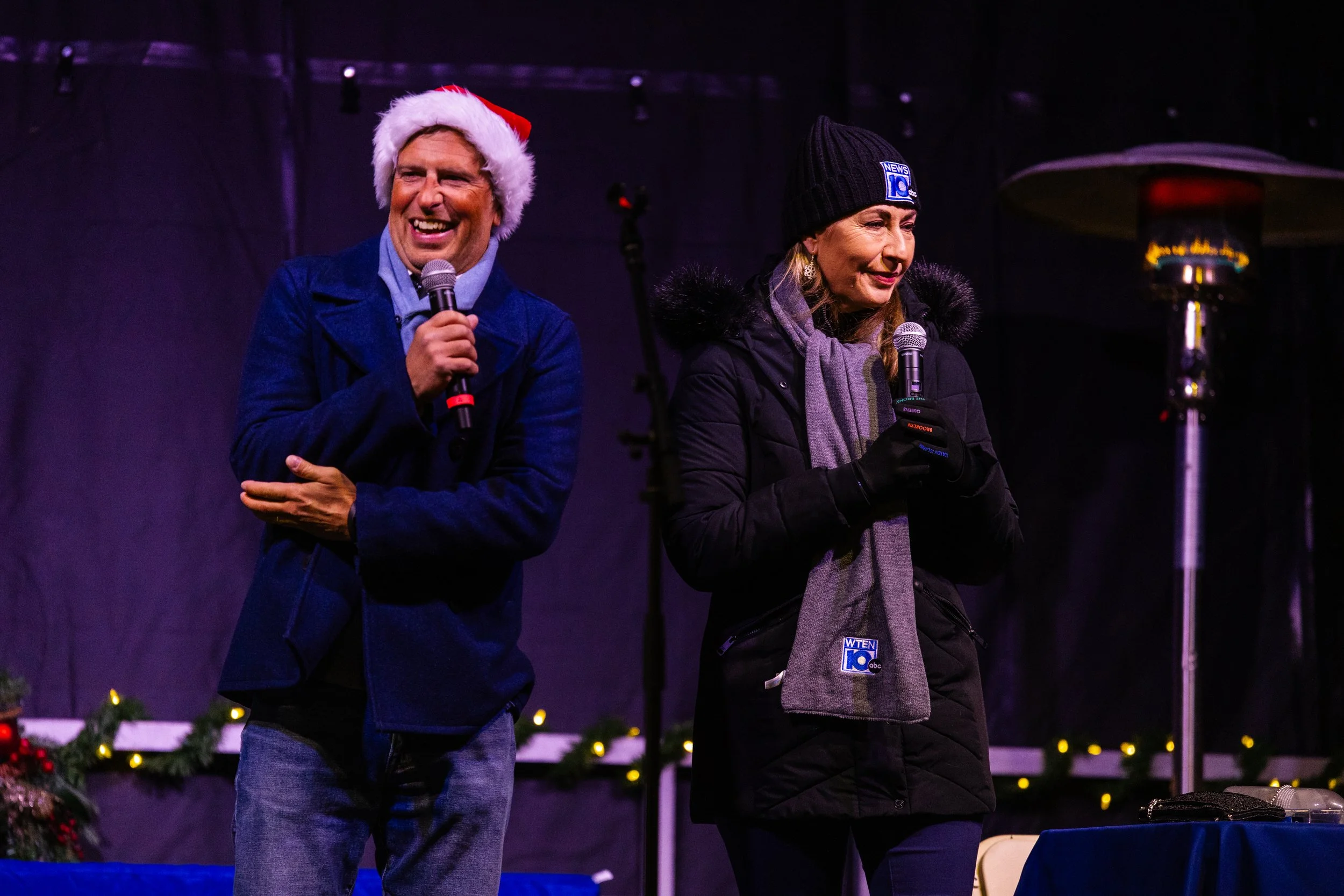 Event hosts speaking on stage during a holiday celebration