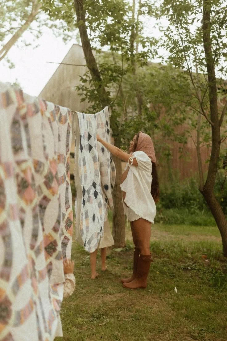 A woman hanging up laundry on a clothesline outdoors in a backyard with trees and a building in the background.