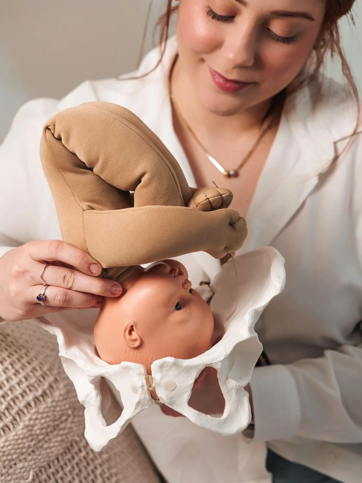 A woman is holding a baby doll in a pelvis-shaped stand, with a nurse's glove on her hand, as part of a medical or educational demonstration.