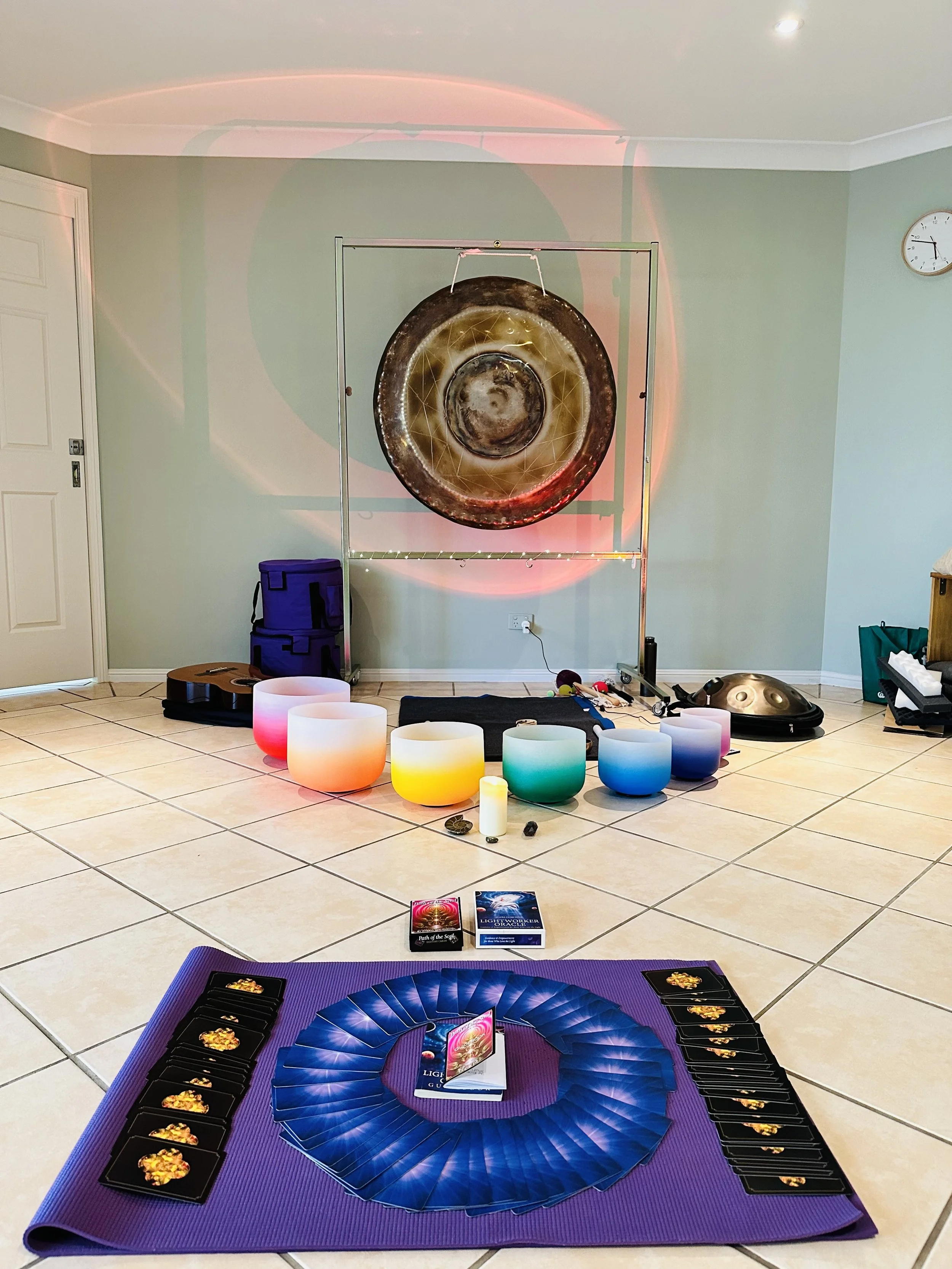 Room set up for a sound healing or meditation session. Includes singing bowls, a gong, musical instruments, candles, and a mat with the cards and guides for the session.