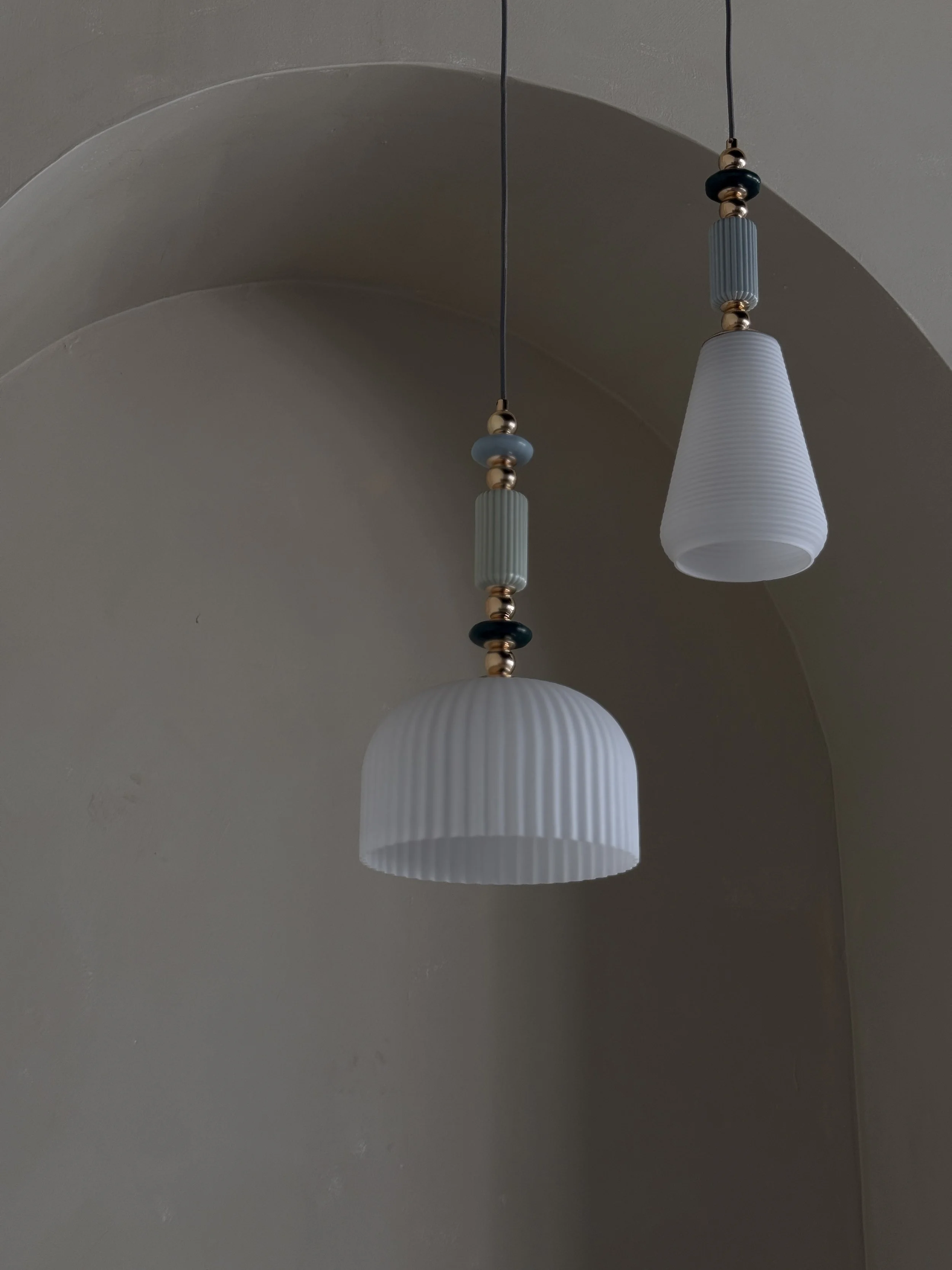 Two pendant light fixtures with ribbed white shades and decorative beads hanging from cords, installed on a ceiling nearby a rounded archway.