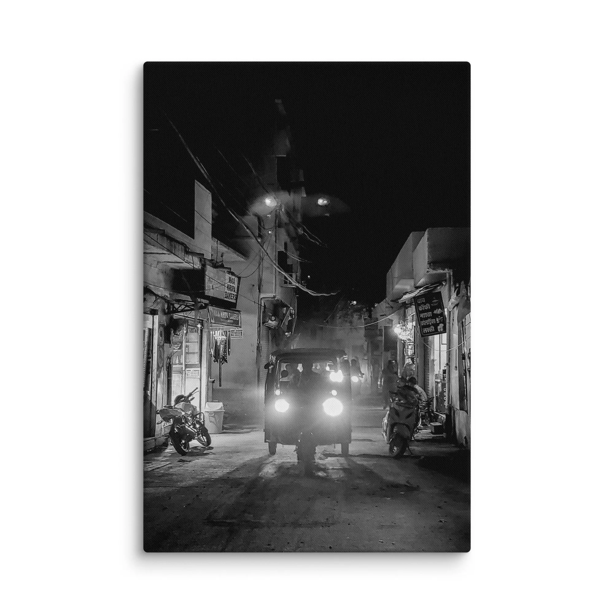 Black-and-white nighttime India alley with glowing tuk-tuk headlights, shops and foggy atmosphere – authentic travel photography canvas print wall art decor