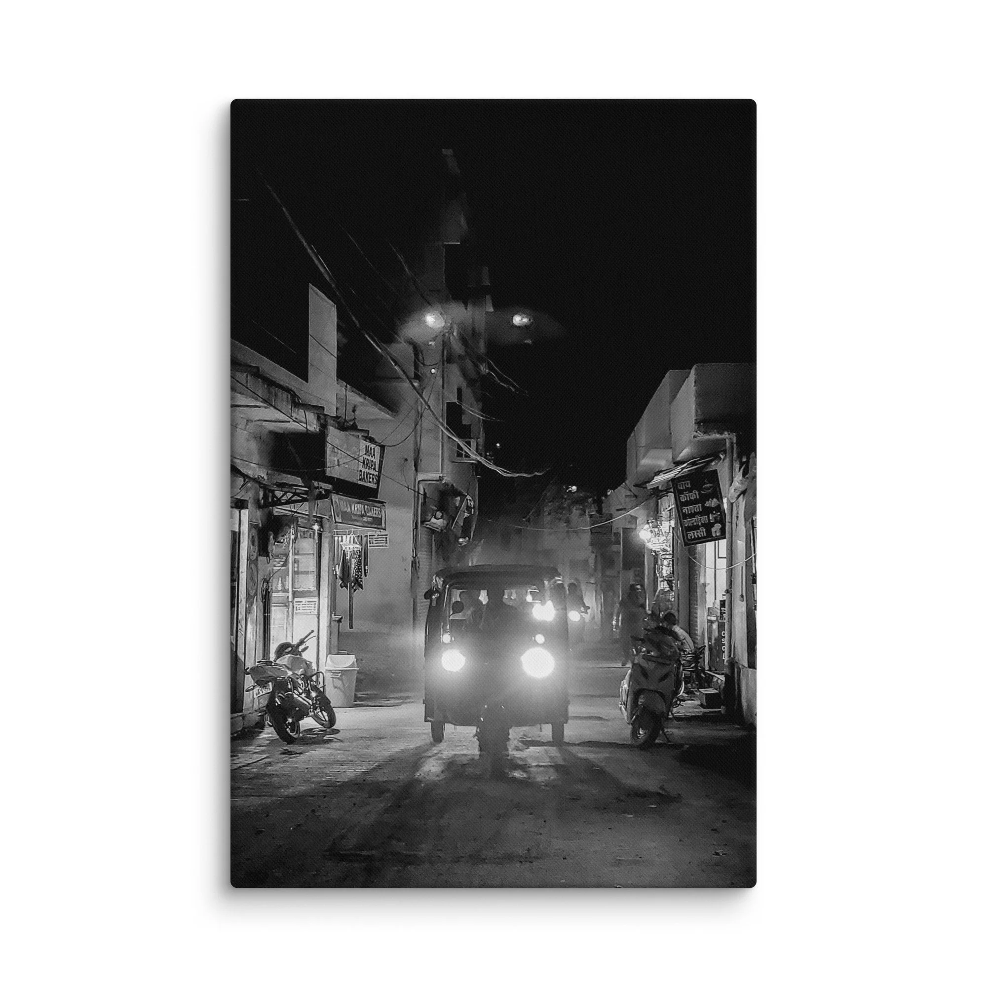 Black-and-white nighttime India alley with glowing tuk-tuk headlights, shops and foggy atmosphere – authentic travel photography canvas print wall art decor