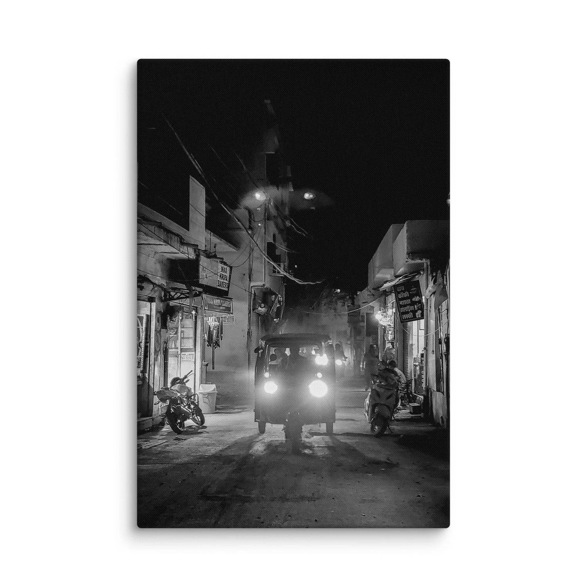 Black-and-white nighttime India alley with glowing tuk-tuk headlights, shops and foggy atmosphere – authentic travel photography canvas print wall art decor