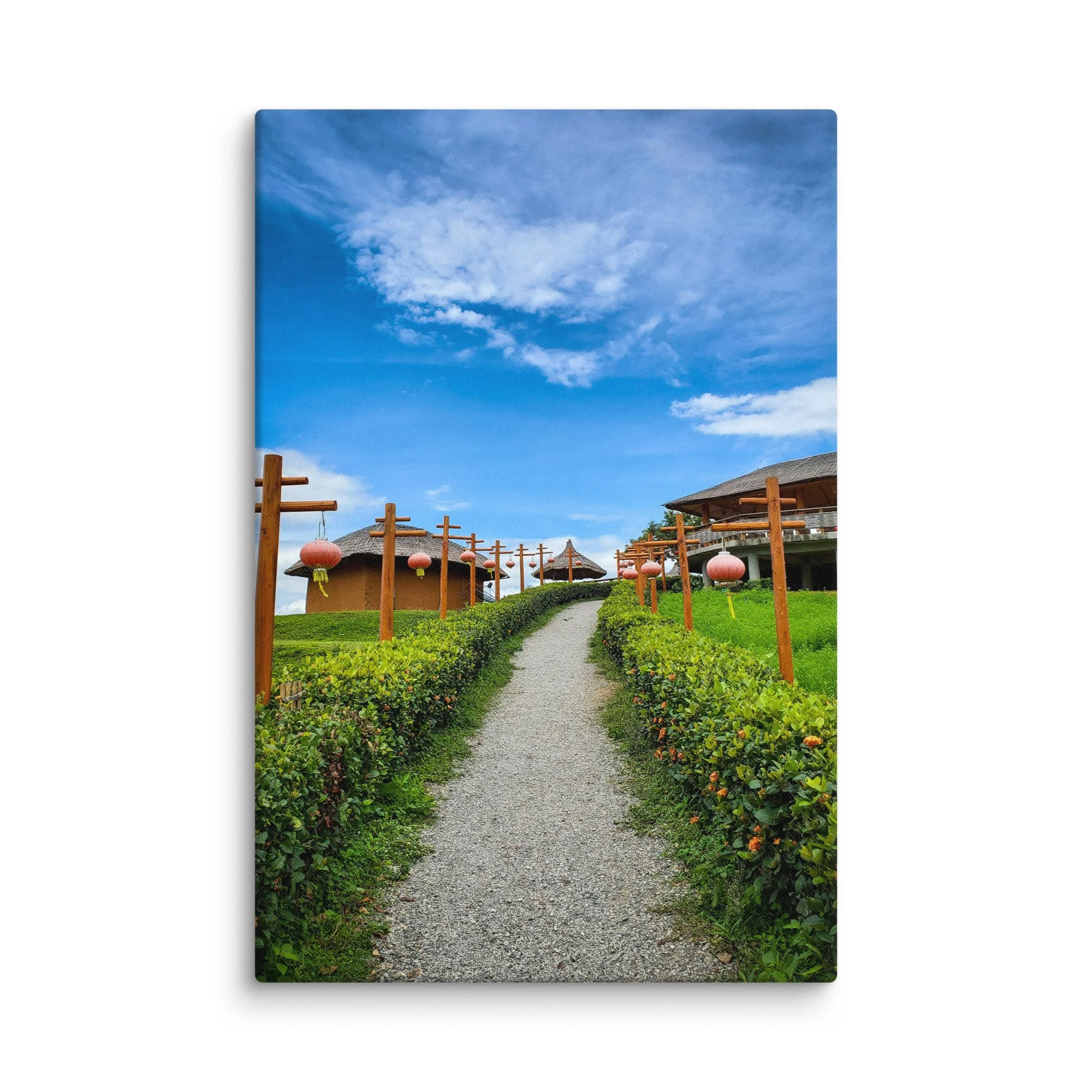 Gravel path lined with pink lanterns leading through thatched-roof resort huts under bright blue sky in Thailand – tropical travel photography canvas print wall art decor