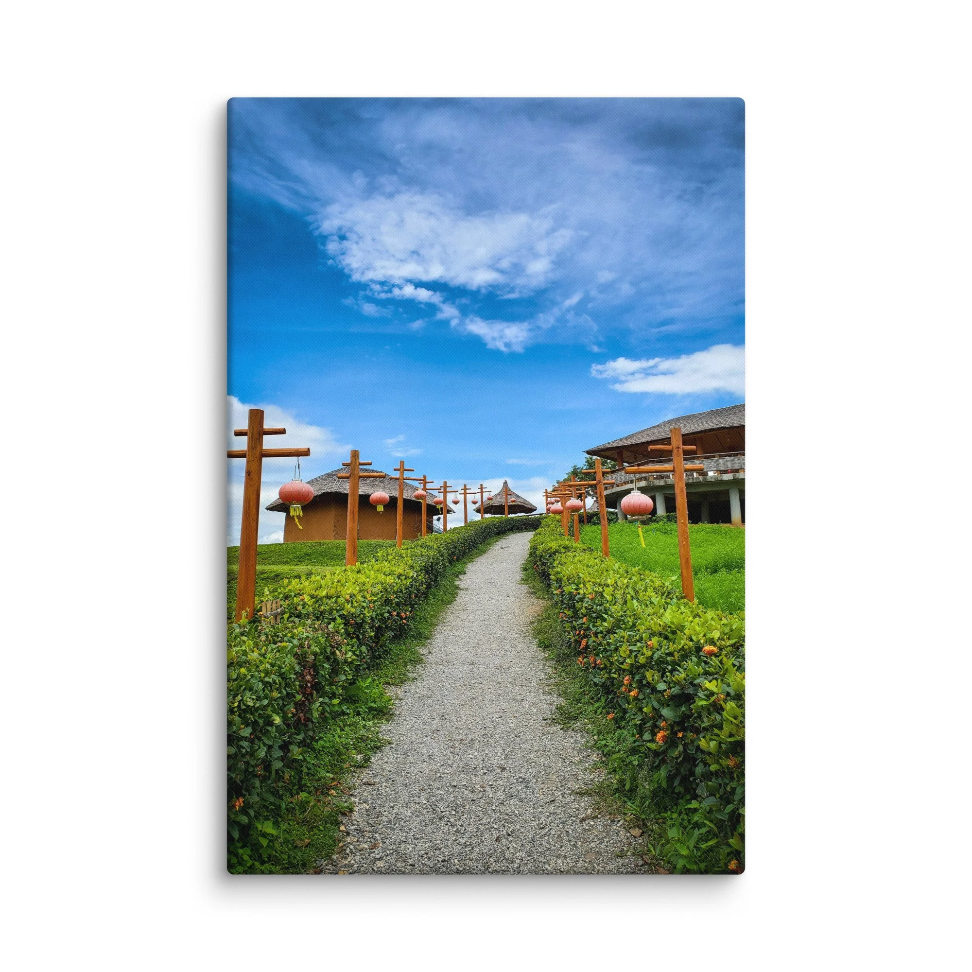 Gravel path lined with pink lanterns leading through thatched-roof resort huts under bright blue sky in Thailand – tropical travel photography canvas print wall art decor