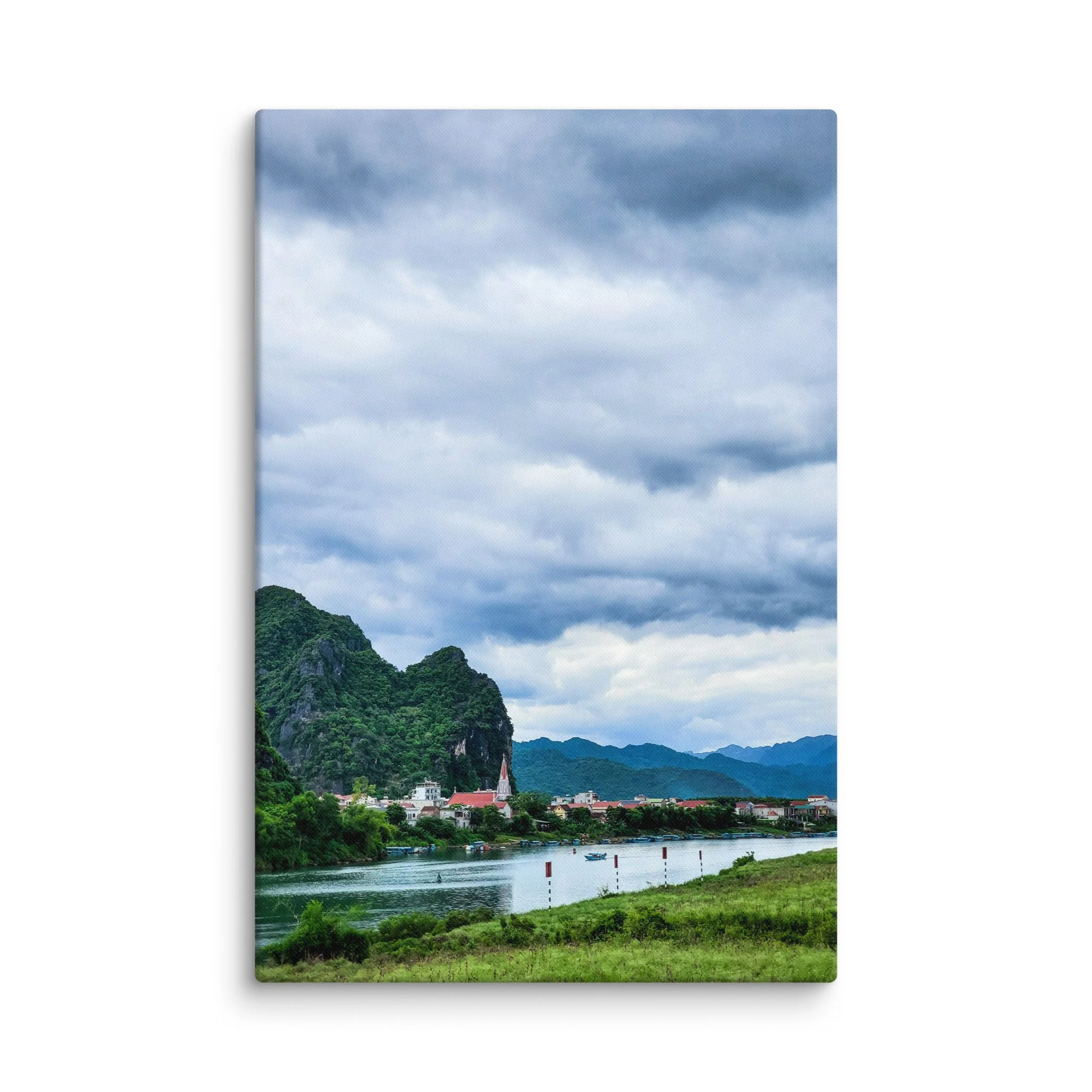 Riverside village with white church steeple along a calm river surrounded by lush green limestone karsts in northern Vietnam under dramatic sky – travel photography canvas print wall art