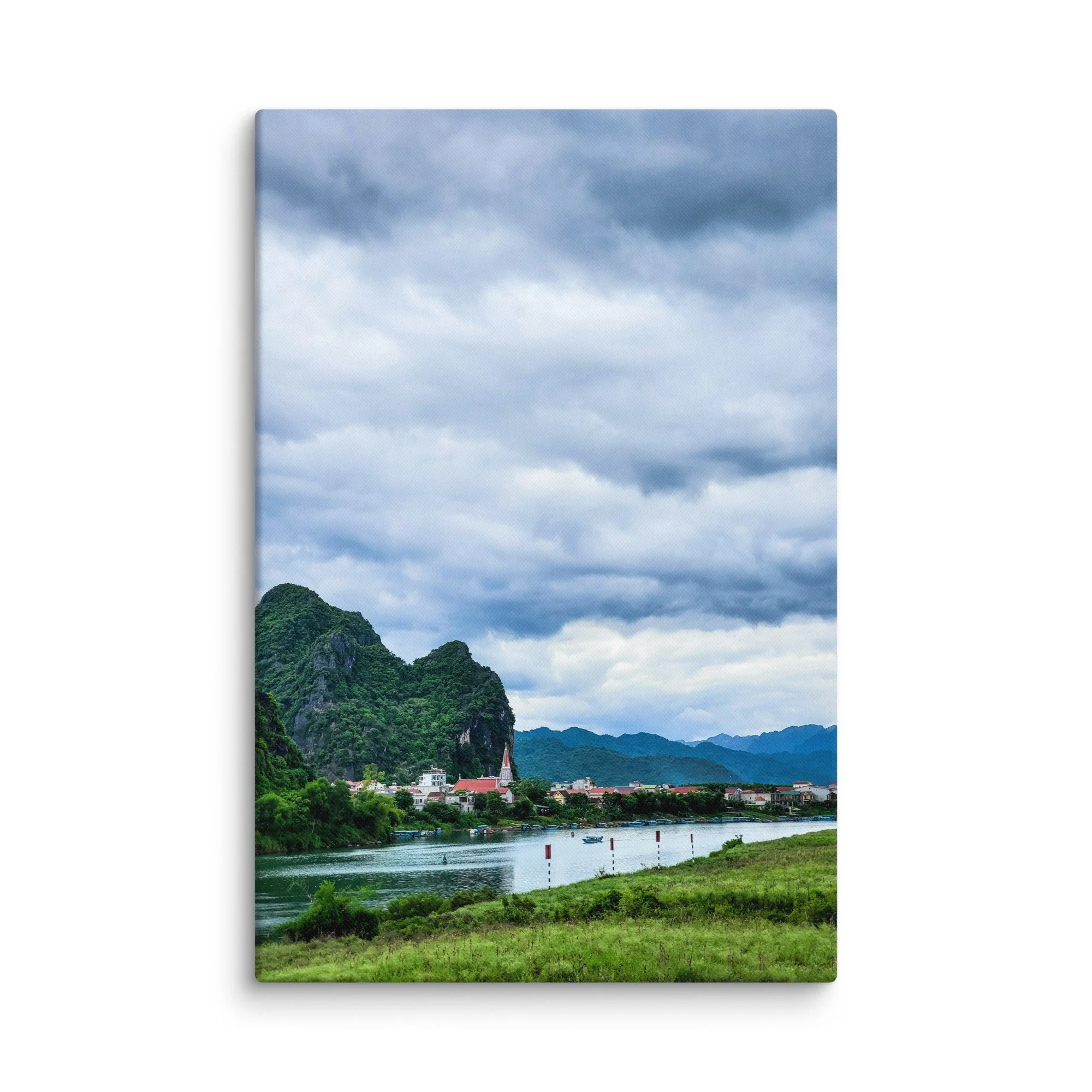 Riverside village with white church steeple along a calm river surrounded by lush green limestone karsts in northern Vietnam under dramatic sky – travel photography canvas print wall art