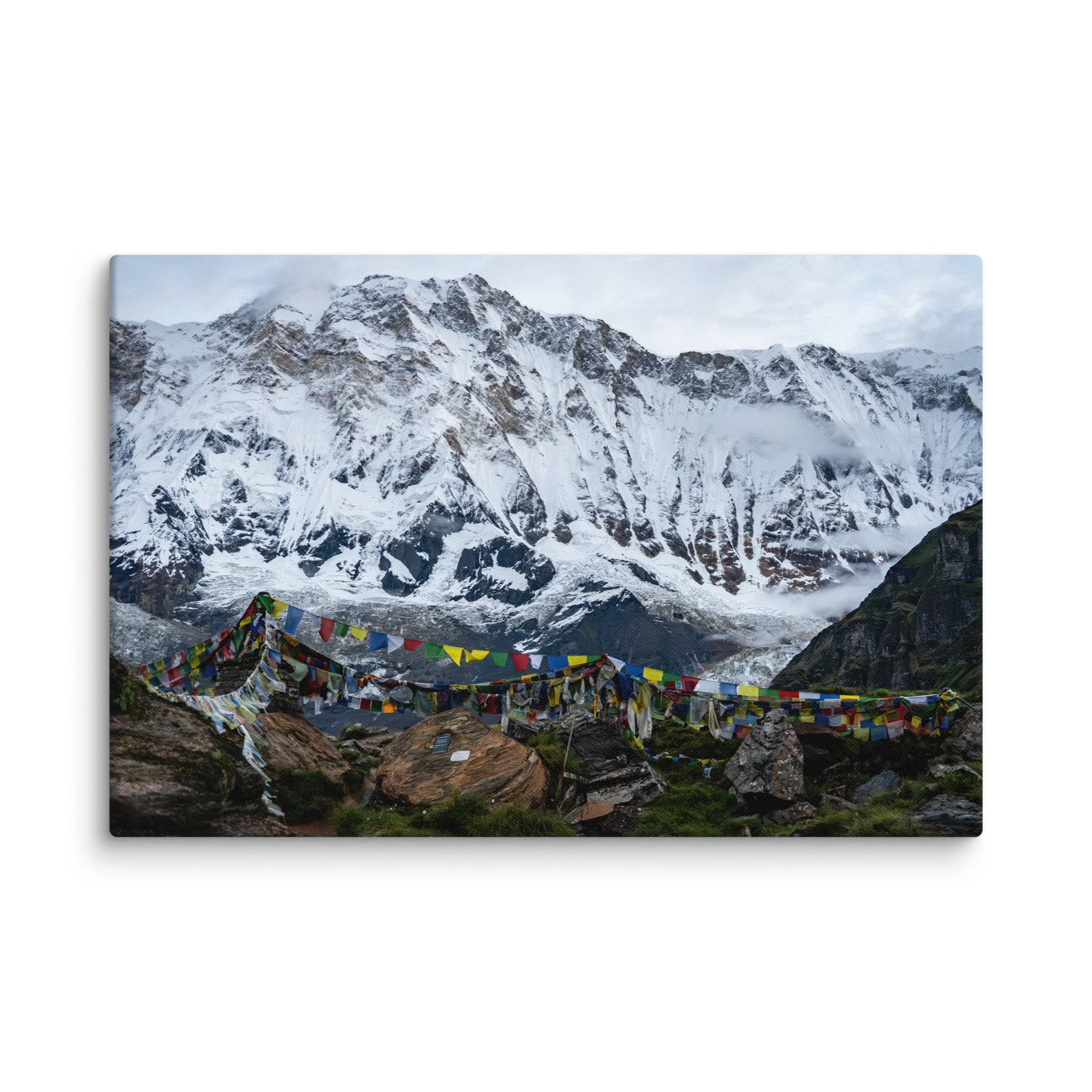 Vibrant multicolored prayer flags in the foreground with towering snow-covered Himalayan peaks and misty sky at Annapurna Base Camp, Nepal – high-altitude spiritual trekking travel