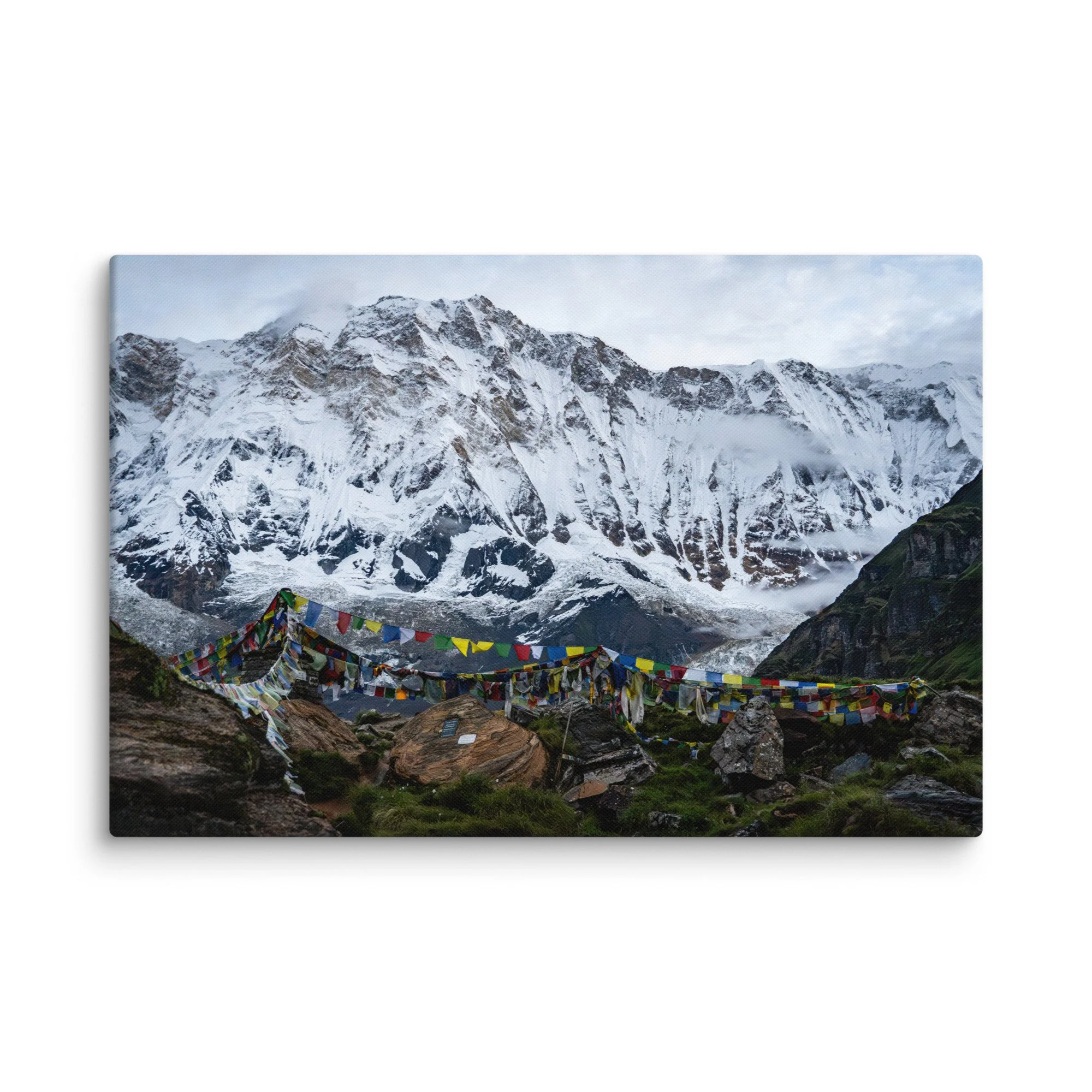 Vibrant multicolored prayer flags in the foreground with towering snow-covered Himalayan peaks and misty sky at Annapurna Base Camp, Nepal – high-altitude spiritual trekking travel