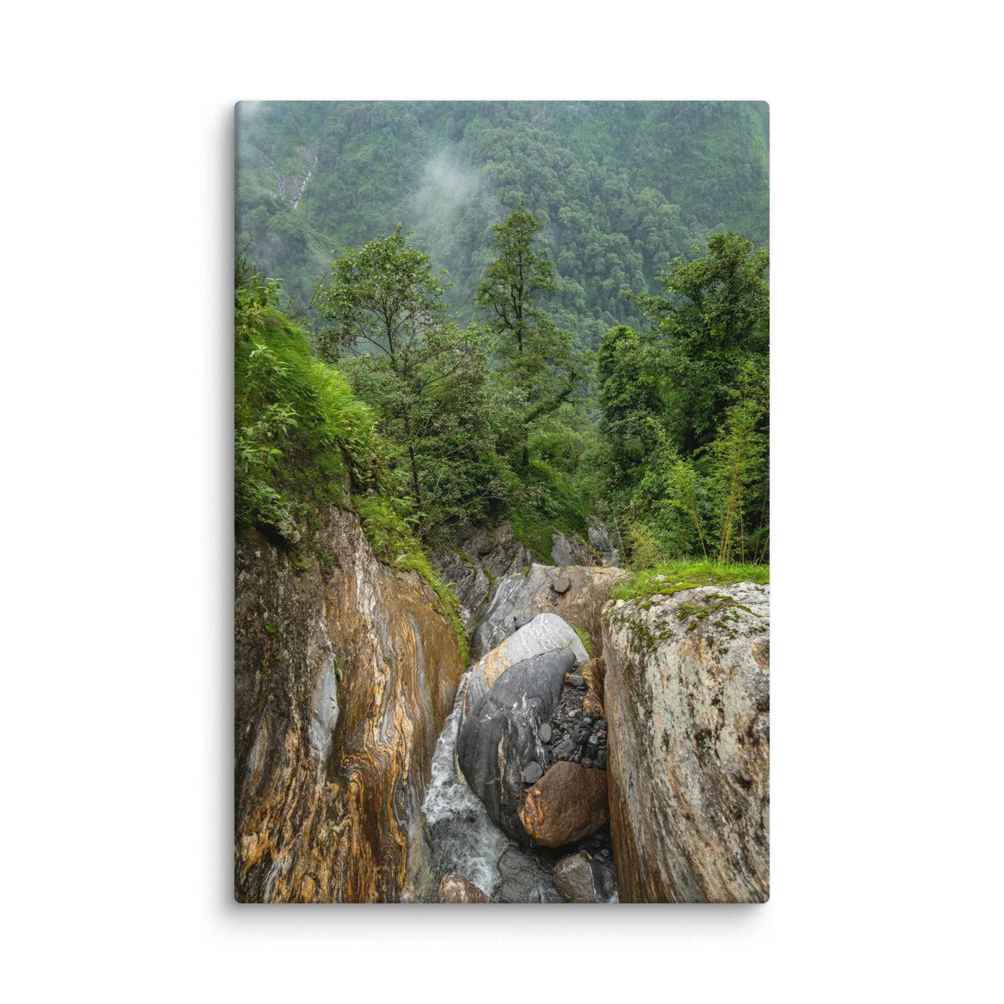Misty jungle stream cascading over colorful boulders in a lush green gorge on the Annapurna Circuit/Base Camp Trek, Nepal, surrounded by dense forest and fog – high-altitude