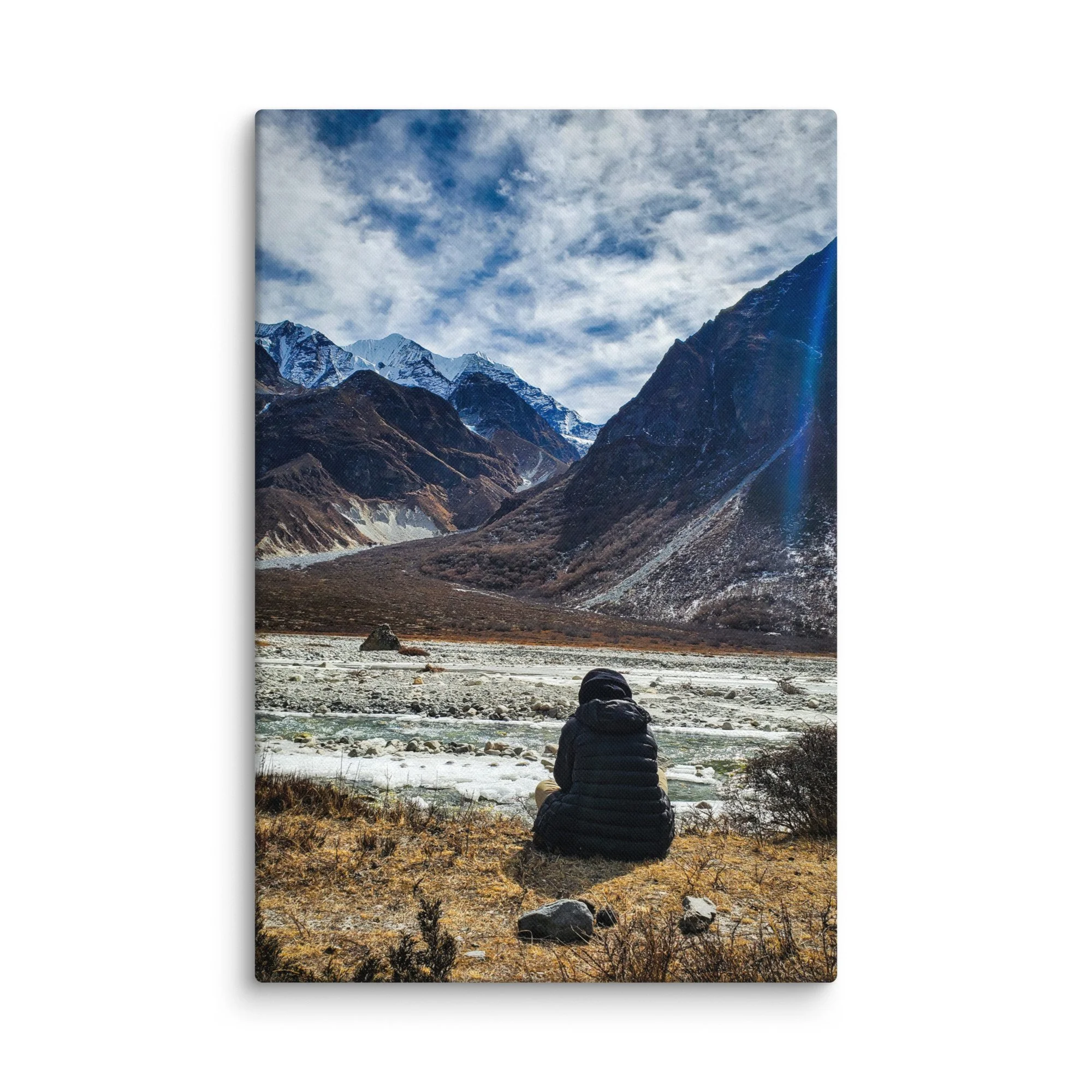 Lone trekker sitting on rocky riverbank in Langtang Valley, Nepal, overlooking turquoise glacial river and majestic snow-capped peaks under blue sky – Himalayan trekking travel