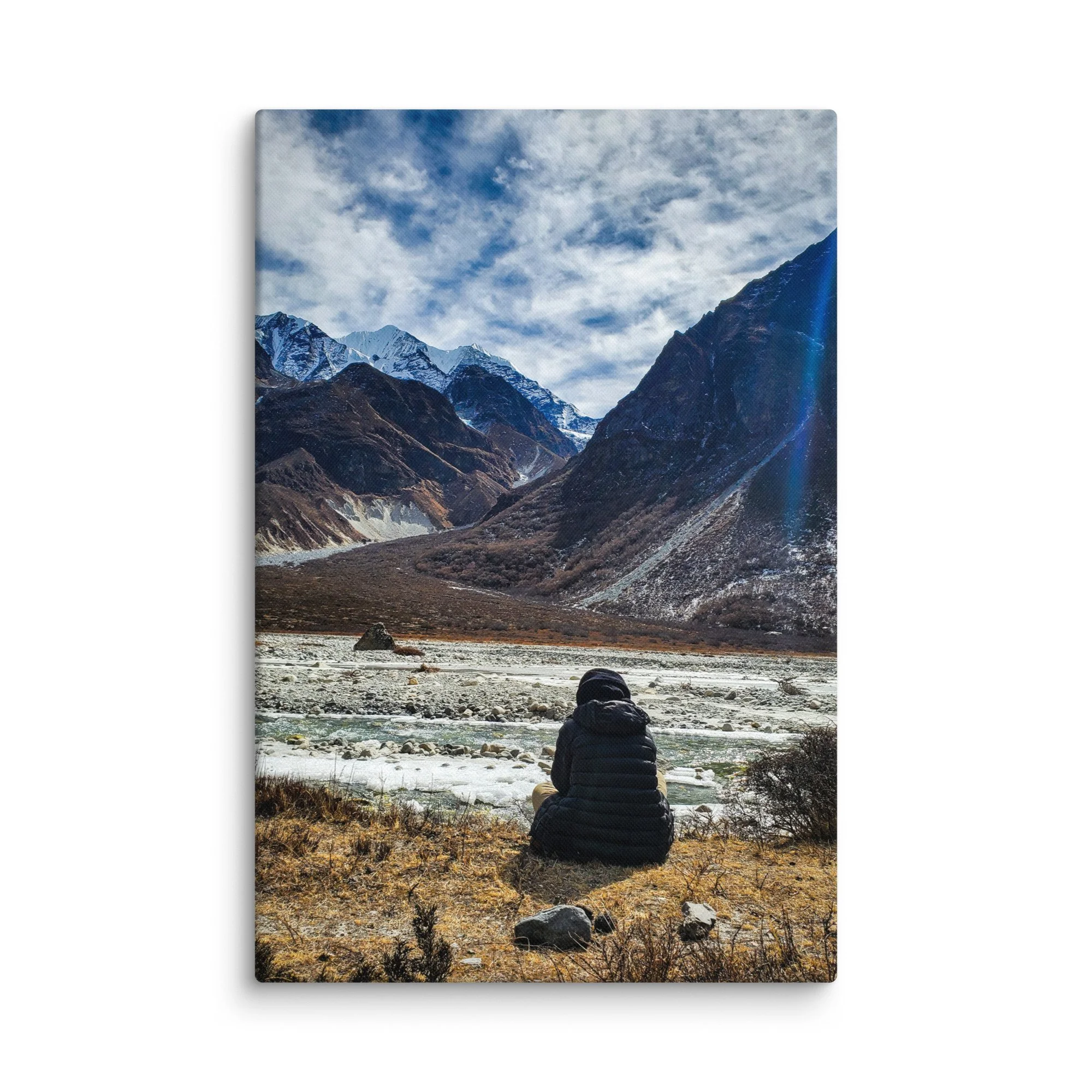 Lone trekker sitting on rocky riverbank in Langtang Valley, Nepal, overlooking turquoise glacial river and majestic snow-capped peaks under blue sky – Himalayan trekking travel