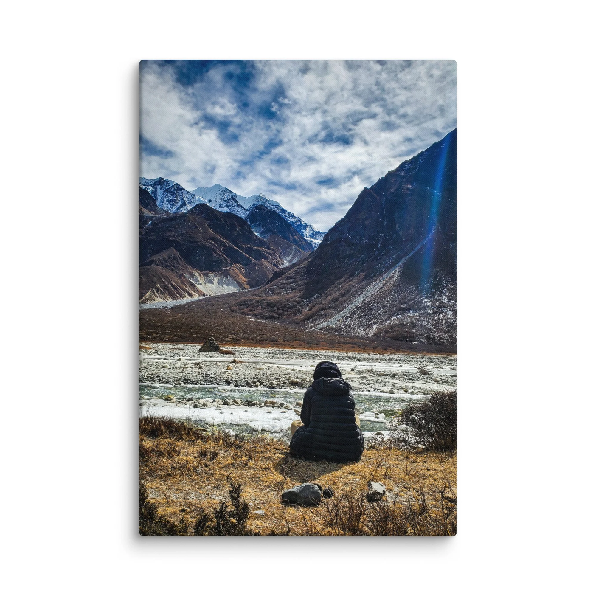 Lone trekker sitting on rocky riverbank in Langtang Valley, Nepal, overlooking turquoise glacial river and majestic snow-capped peaks under blue sky – Himalayan trekking travel
