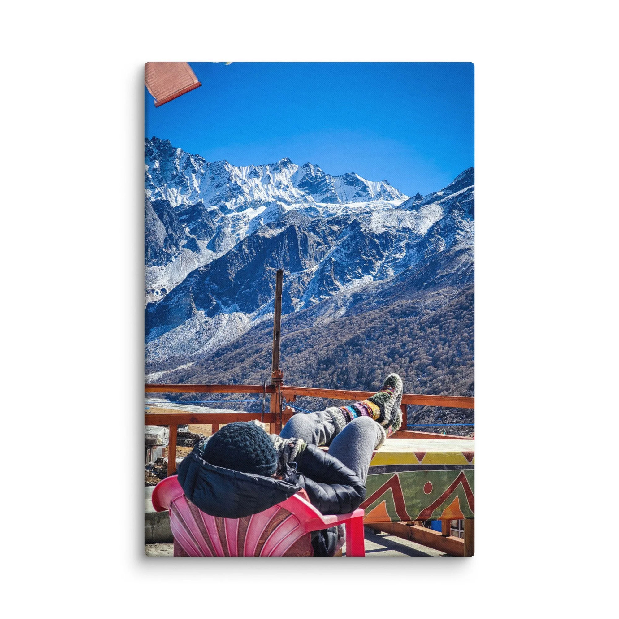 Trekker relaxing on colorful rooftop bench in Langtang Valley, Nepal, with feet up in wool socks and majestic snow-capped Himalayan peaks under brilliant blue sky – trekking travel