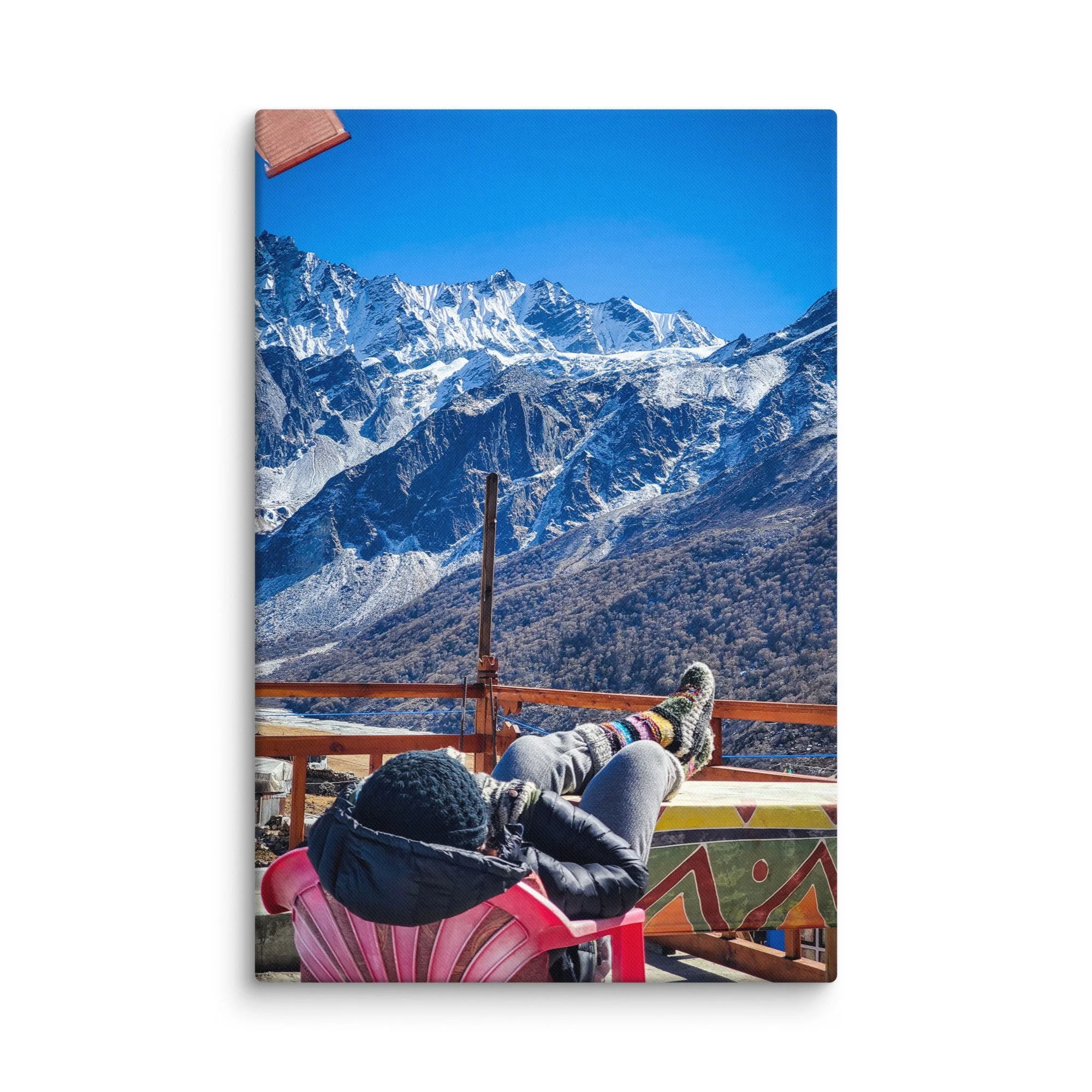 Trekker relaxing on colorful rooftop bench in Langtang Valley, Nepal, with feet up in wool socks and majestic snow-capped Himalayan peaks under brilliant blue sky – trekking travel