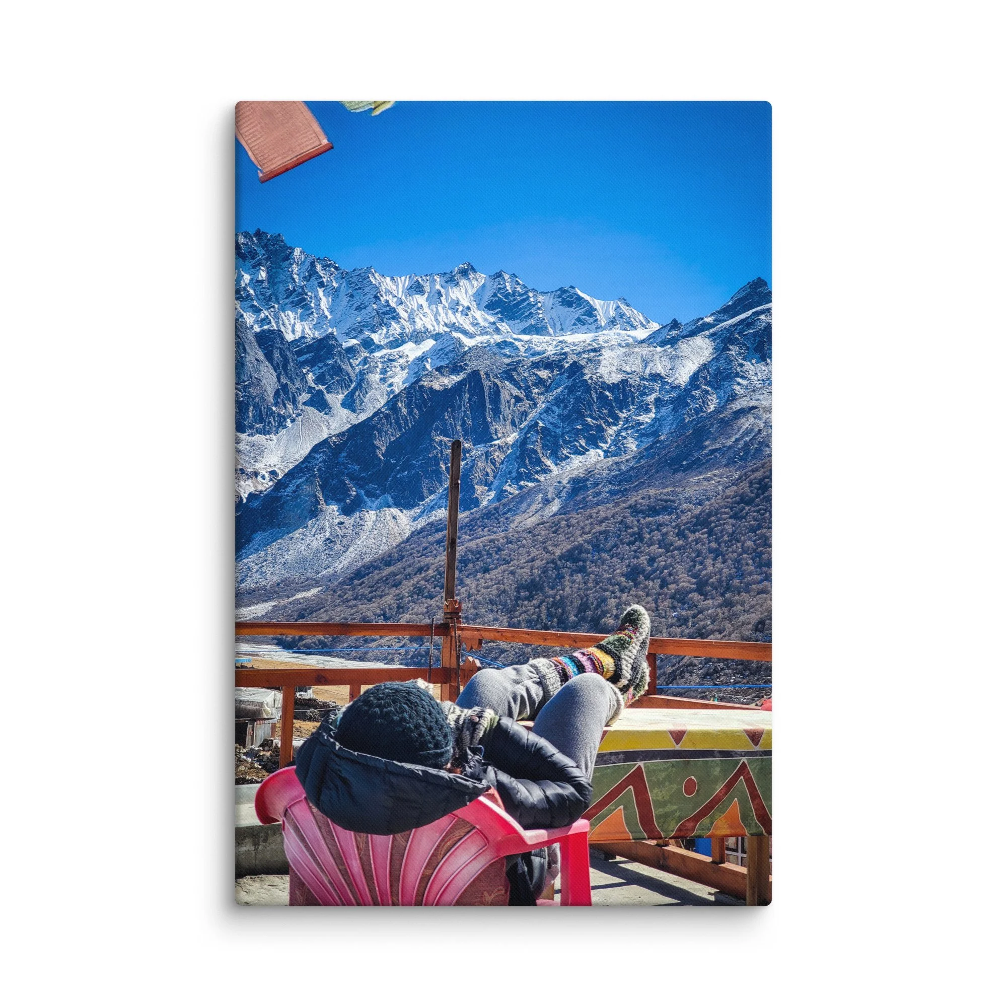 Trekker relaxing on colorful rooftop bench in Langtang Valley, Nepal, with feet up in wool socks and majestic snow-capped Himalayan peaks under brilliant blue sky – trekking travel