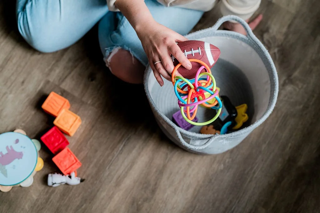 Angela cleans up toddler toys from the floor representing "mom-life" and how she loves to help service providers who help moms' lives a little easier with their unique skills